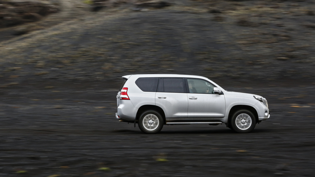 Silberner SUV fährt auf dunklem, steinigem Gelände. Seitenansicht des Fahrzeugs in Bewegung.