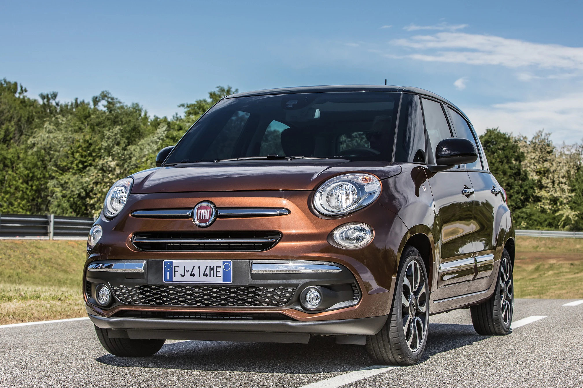 Ein brauner Fiat 500L steht auf einer Straße, umgeben von Bäumen. Sicht auf die Front und Seite des Autos.