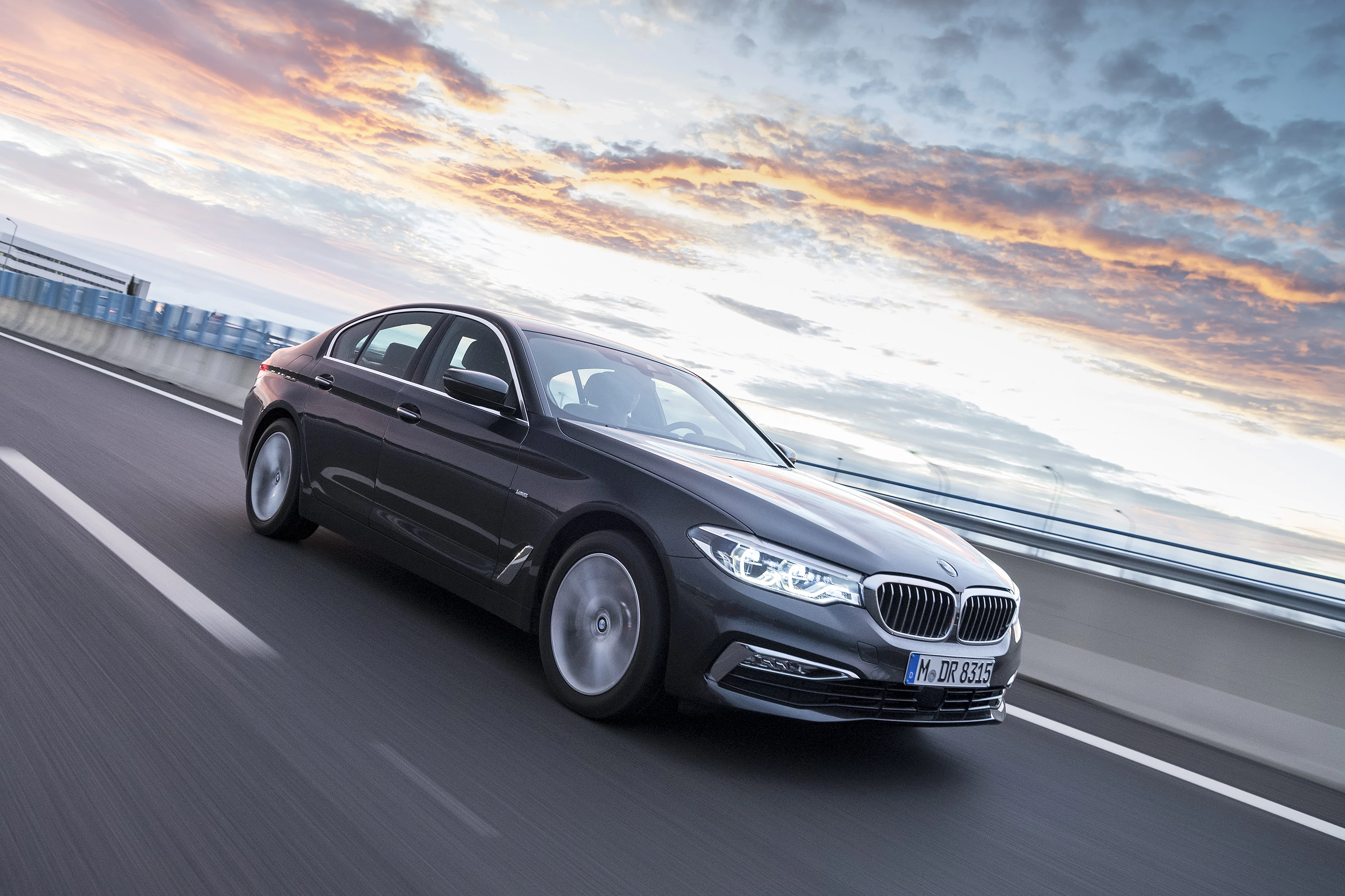 Schwarzer BMW fährt bei Sonnenuntergang auf einer Autobahn, dynamische Bewegungseffekte, Himmel mit Wolken im Hintergrund.