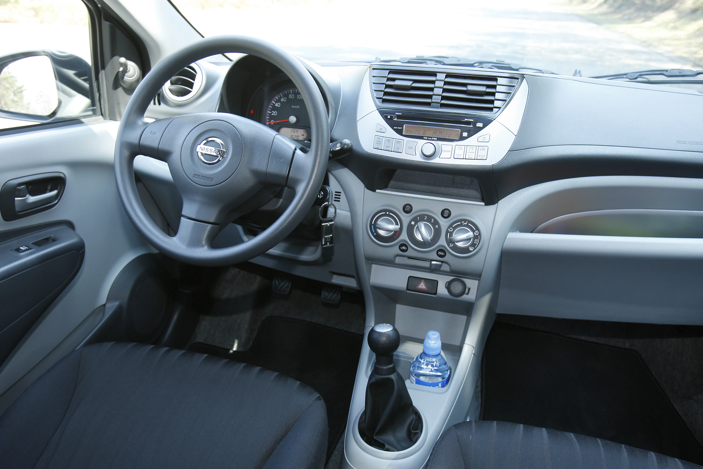 Innenraum eines Autos mit Lenkrad, Schalthebel und Armaturenbrett. Eine Wasserflasche steht im Getränkehalter.