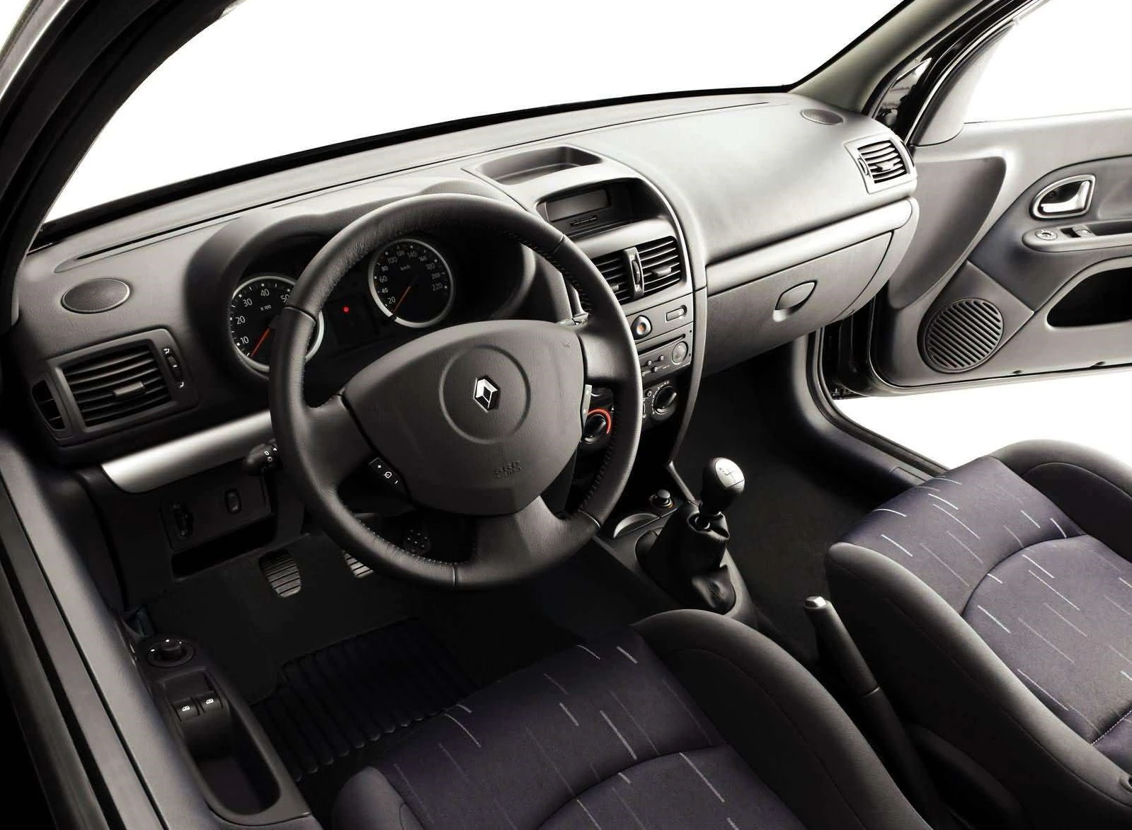 Innenraum eines Autos mit schwarzem Armaturenbrett, Lenkrad und Schalthebel. Zwei graue Sitze sind sichtbar.