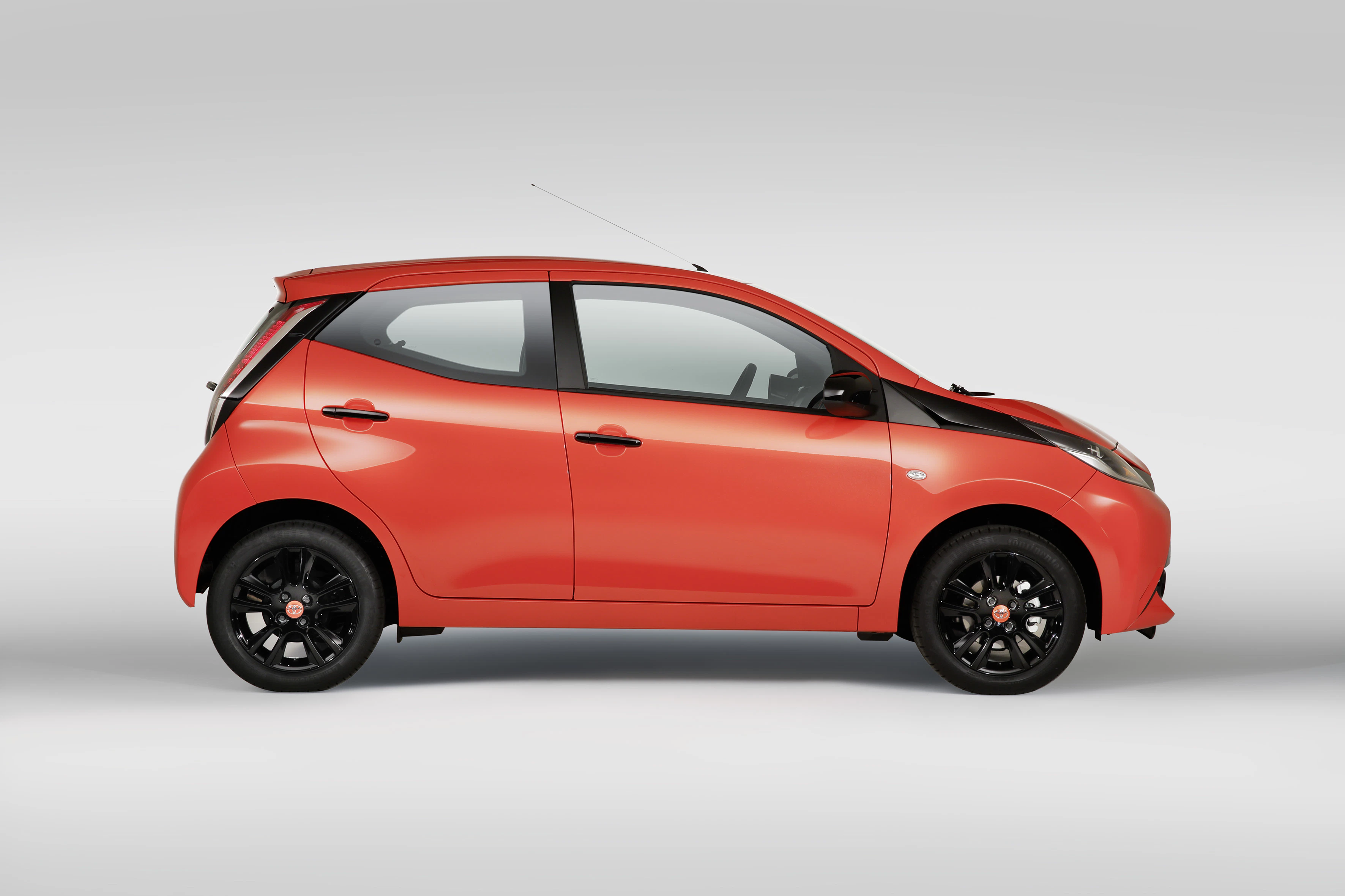 Rotes, modernes Stadtauto mit schwarzen Felgen, Seitenansicht auf grauem Hintergrund.