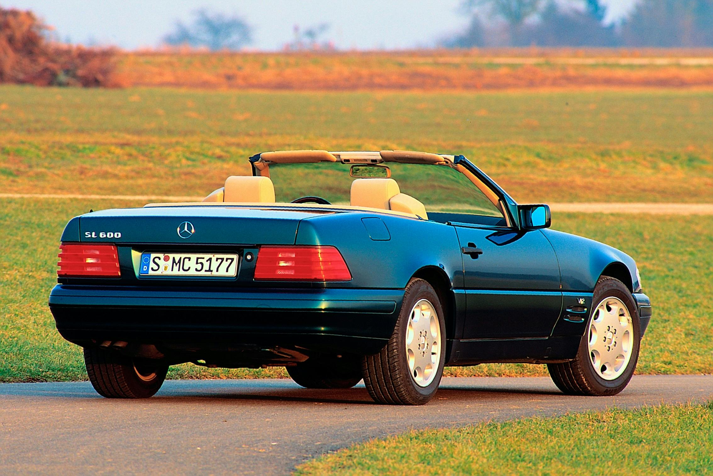 Blauer Mercedes-Benz SL 600 Cabrio der 1990er Jahre auf einer ländlichen Straße bei Sonnenuntergang, mit offenen Verdeck und hellem Innenraum.