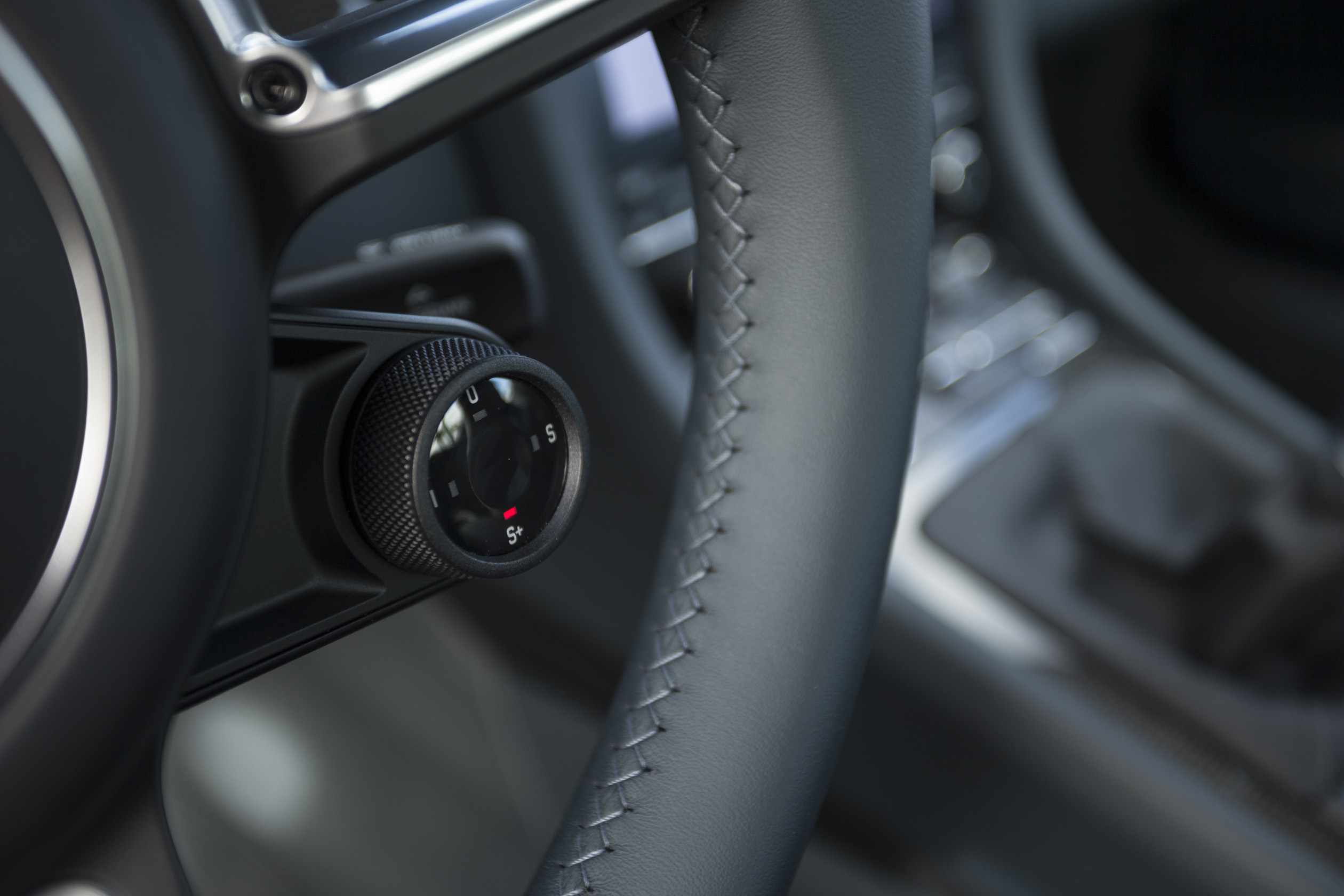 Nahaufnahme eines grau-schwarzen Lenkrads mit sichtbarem Drehknopf und Ledernähten in einem Auto-Innenraum.
