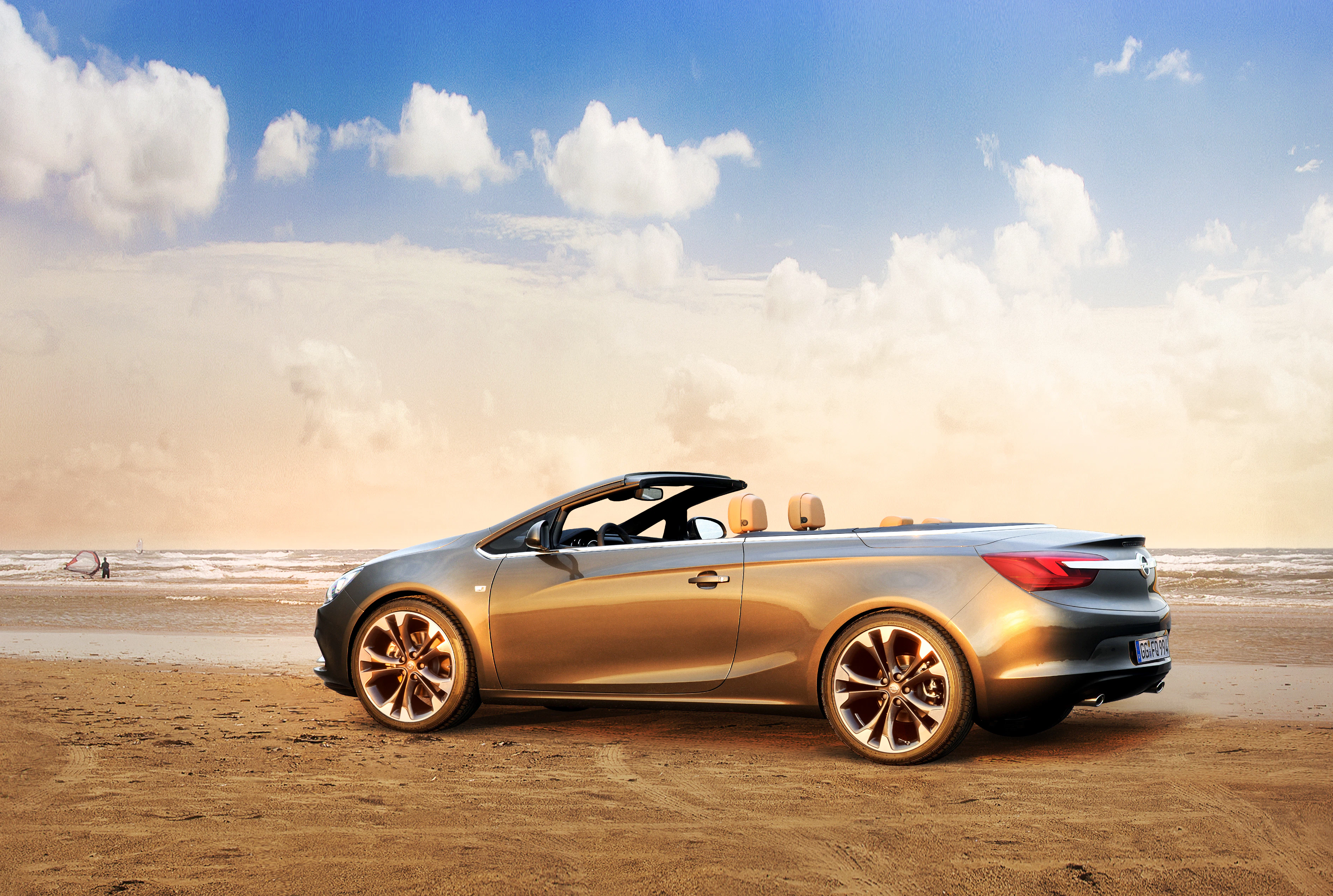 Silbernes Cabrio parkt am Sandstrand bei Sonnenuntergang, blauer Himmel mit Wolken im Hintergrund.