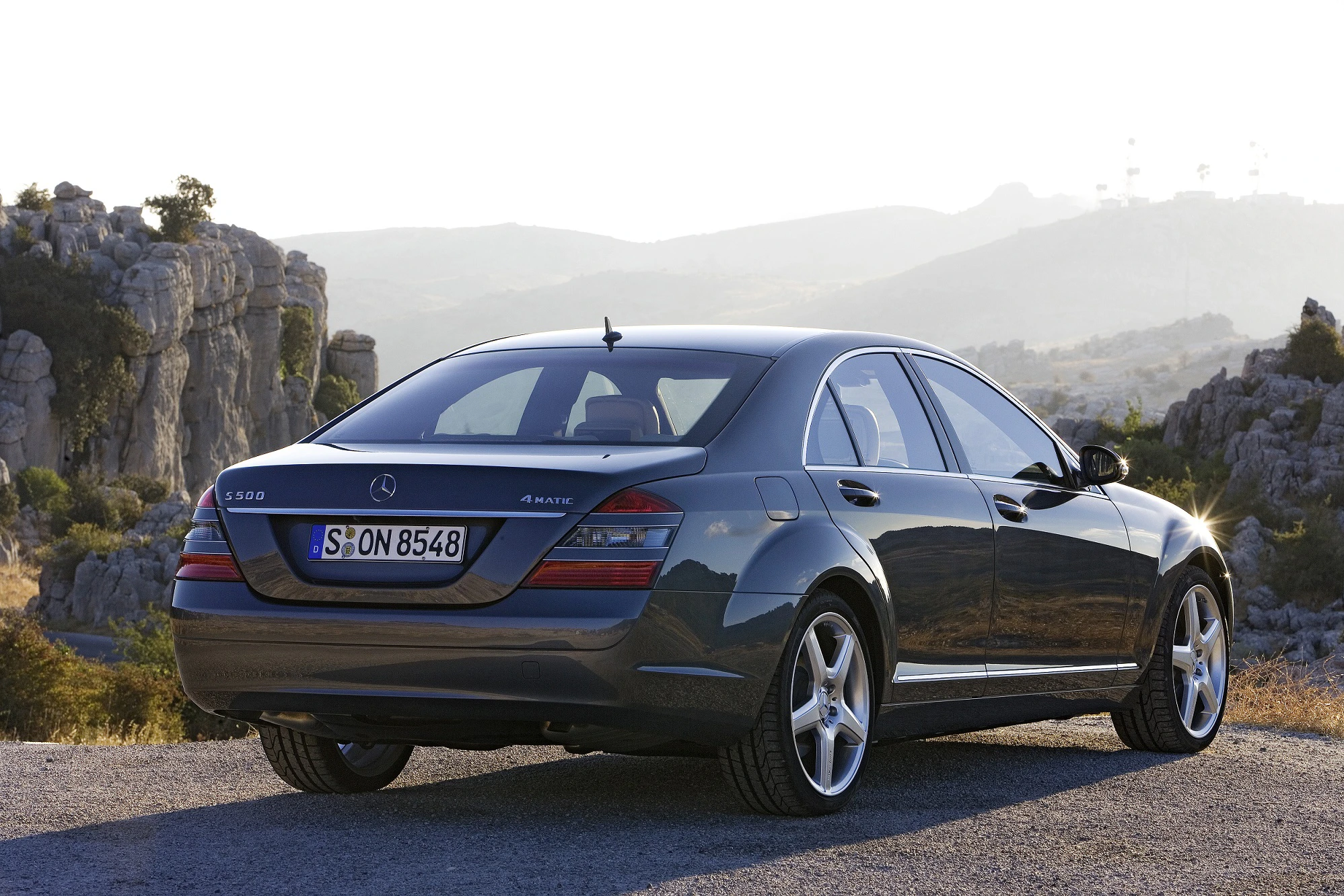 Luxuriöser grauer Mercedes-Benz Sedan, geparkt vor einer felsigen Landschaft bei Sonnenuntergang.