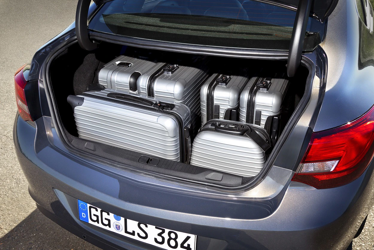 Kofferraum eines Autos mit fünf silbernen Hartschalenkoffern gefüllt. Das Fahrzeug steht auf einer asphaltierten Fläche.