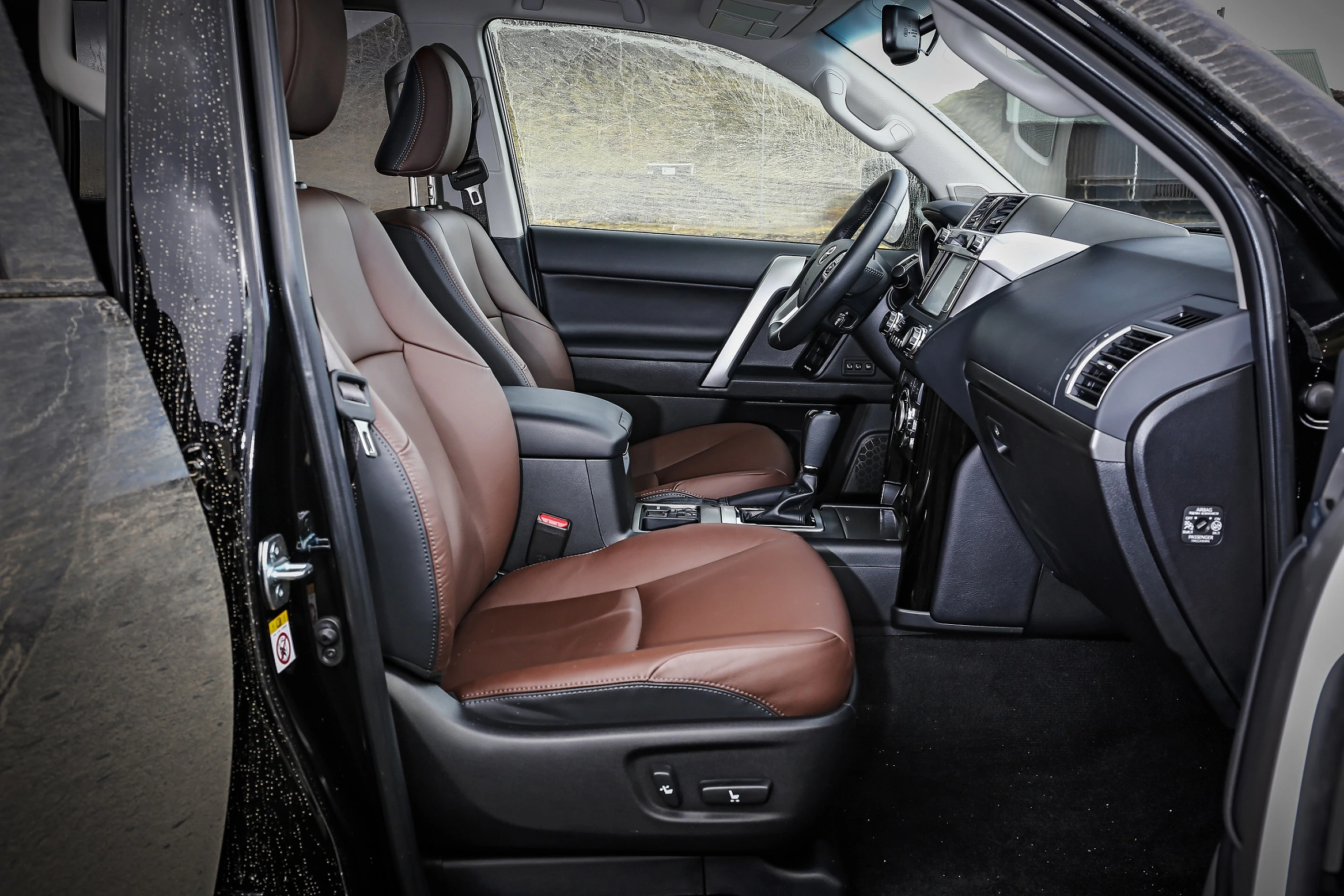 Innenraum eines Autos mit braunen Ledersitzen und modernem Armaturenbrett. Die Tür steht offen, zeigt ein sauberes und elegantes Design.