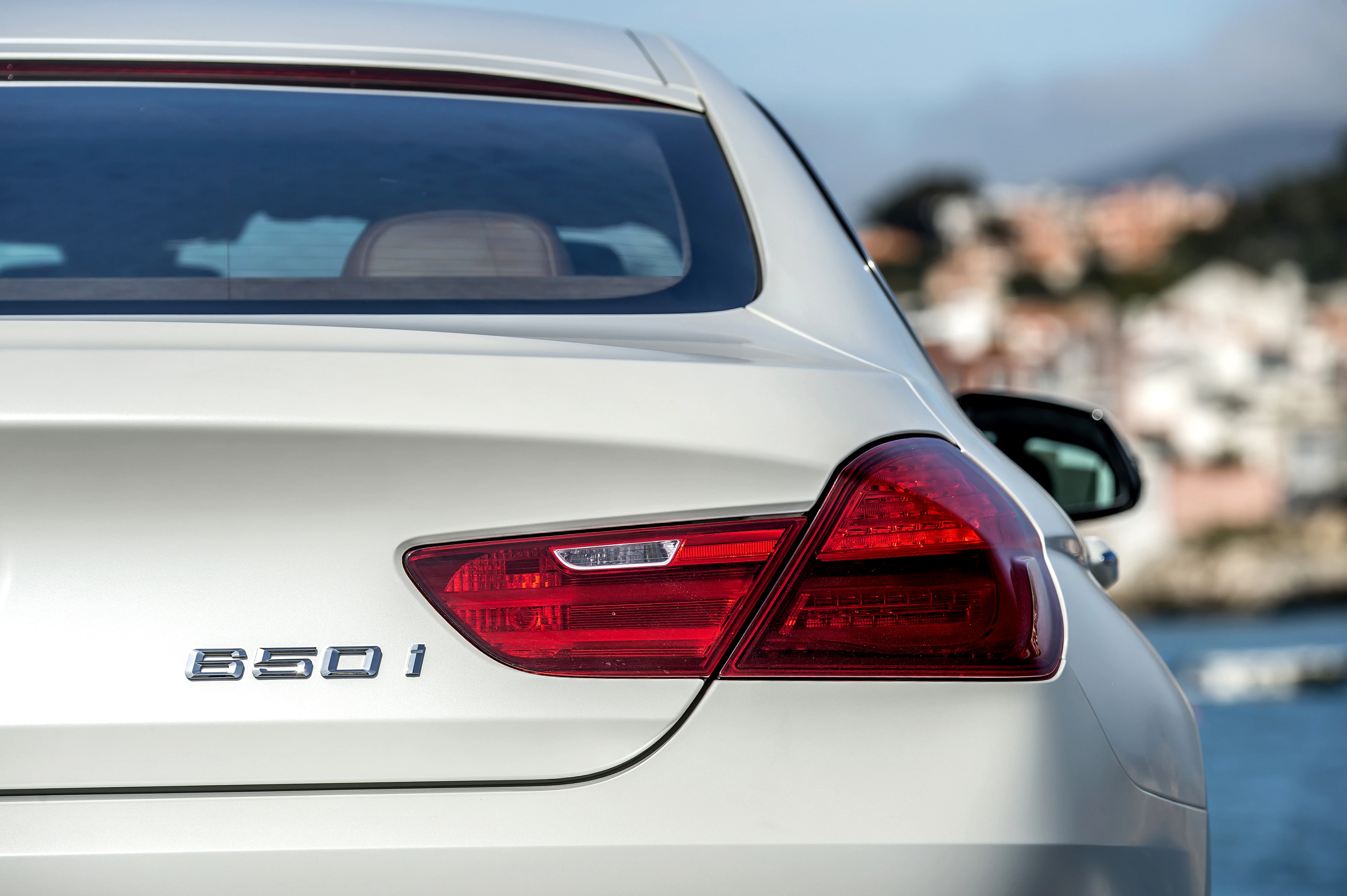 Rückansicht eines weißen BMW 650i mit klaren Rückleuchten. Im Hintergrund unscharfe Stadtlandschaft.