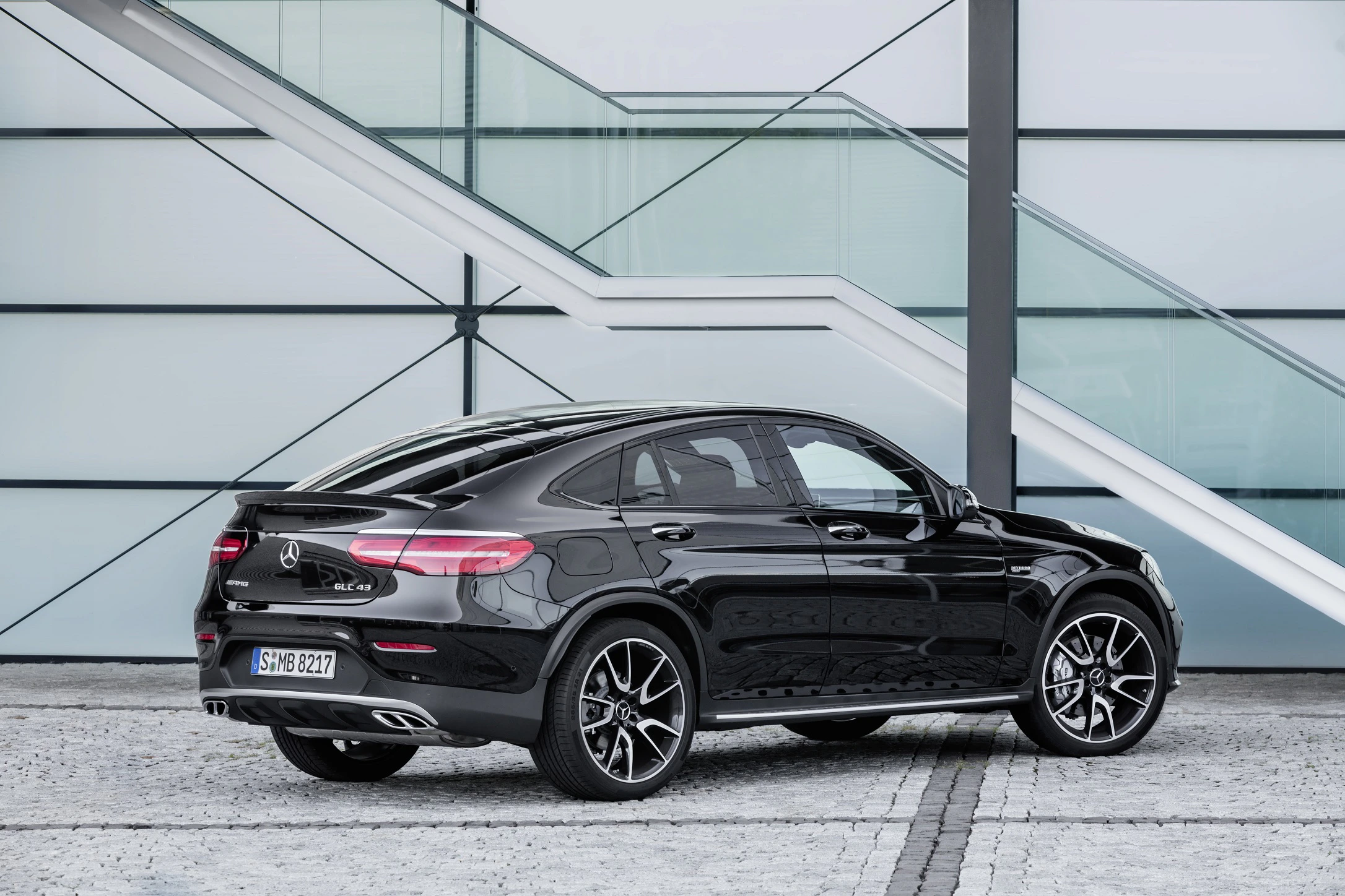 Schwarzes SUV-Coupé vor moderner Glasfassade, seitlich von hinten fotografiert, mit eleganten Linien und stilvollen Felgen.