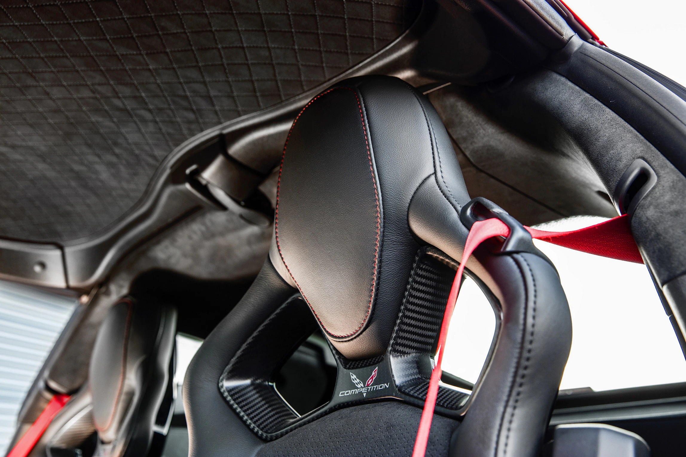 Rennwagensitz mit schwarzem Leder, roten Nähten und Renngurten im Innenraum eines Autos, von unten fotografiert.
