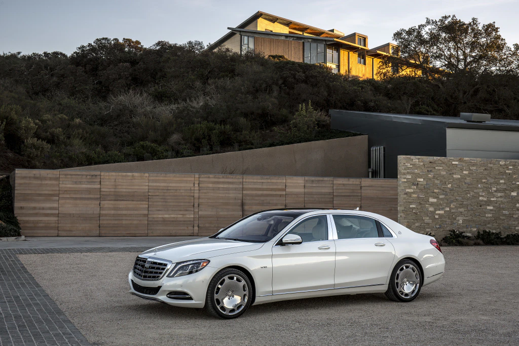 Ein weißer Luxuslimousine steht auf einer gepflasterten Auffahrt vor einem modernen Haus in einer bewaldeten Gegend.