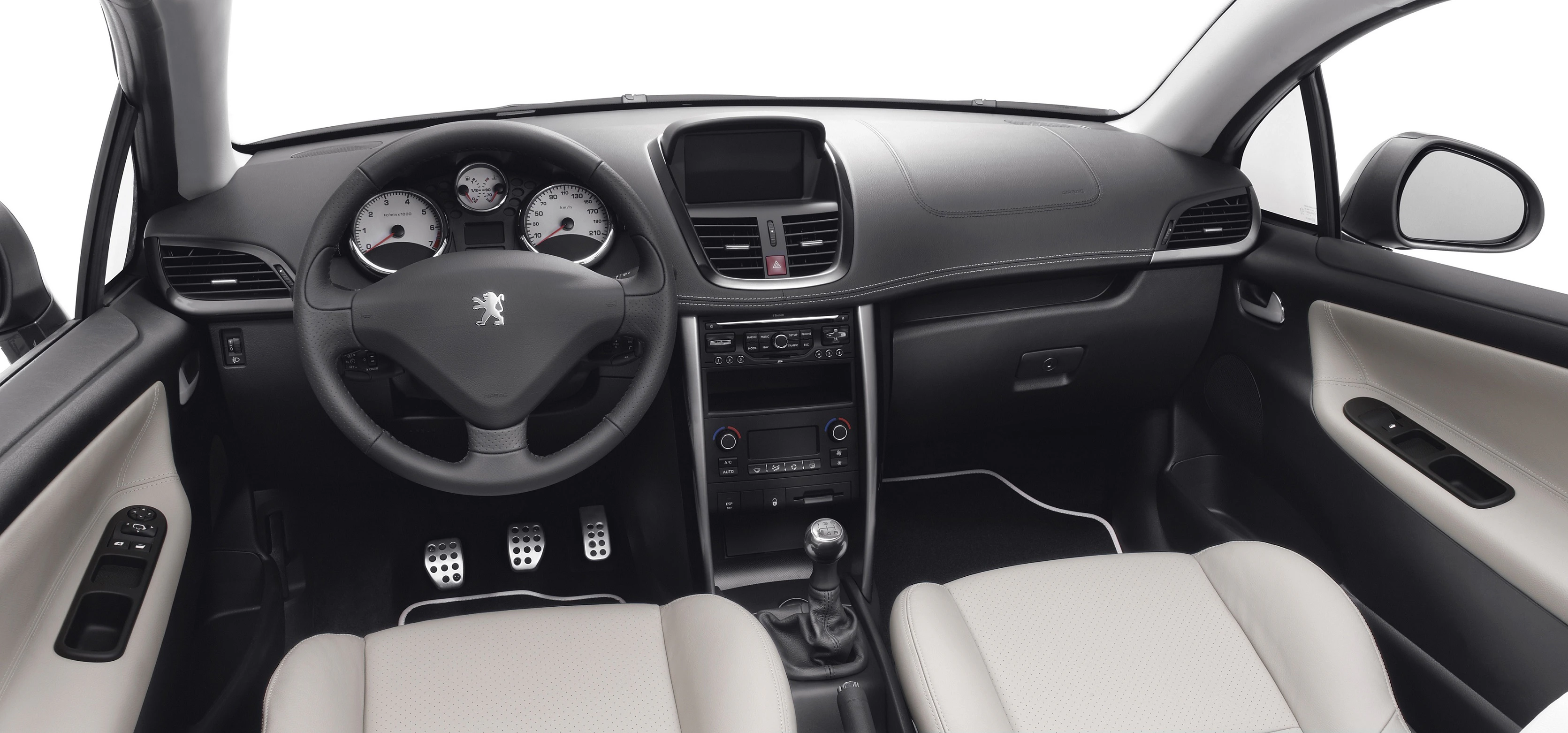 Innenraum eines Autos mit schwarzem Armaturenbrett, Lenkrad mit Löwenemblem, zwei beigefarbenen Sitzen und Schaltgetriebe.