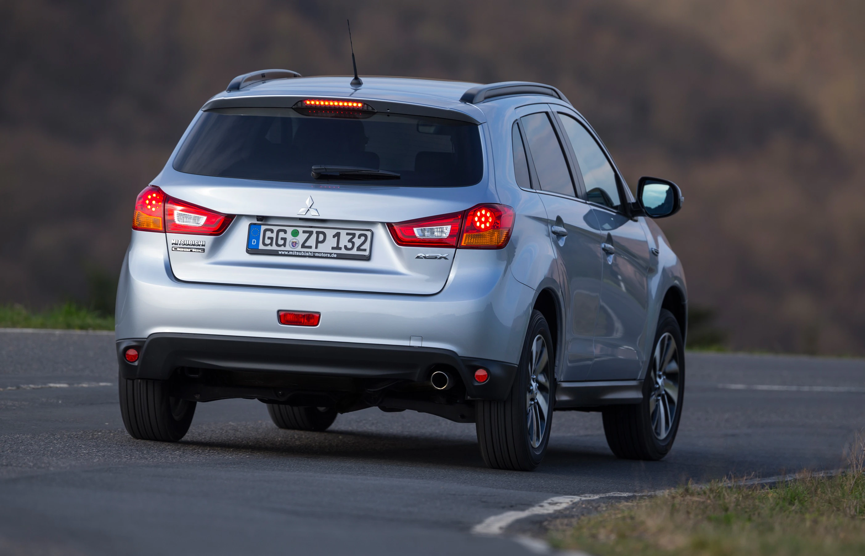 Silberner SUV auf kurviger Landstraße von hinten, fährt bergauf.