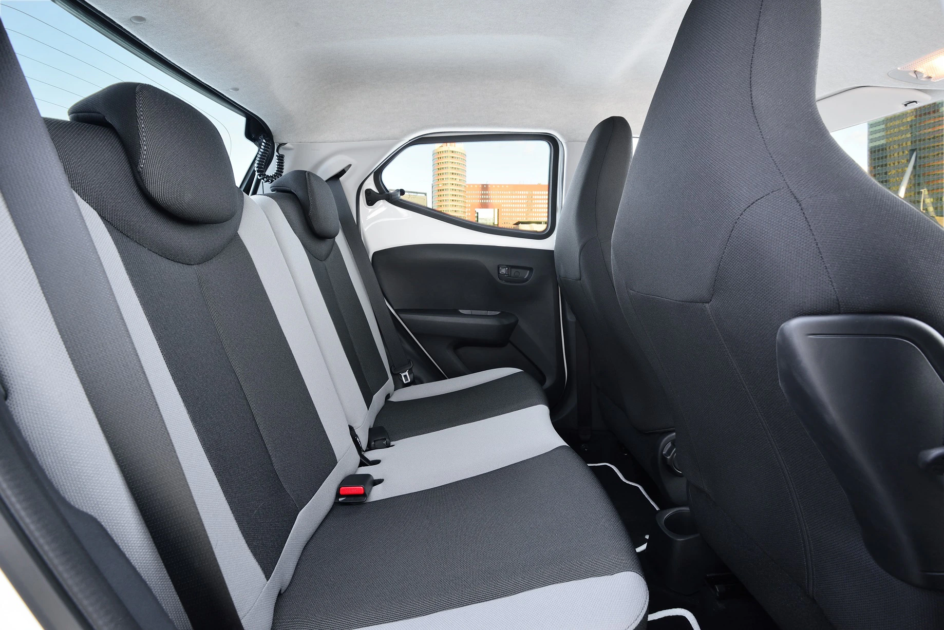 Innenraum eines Autos mit zwei Sitzreihen. Die Sitze sind schwarz-grau gepolstert. Fenster und Tür auf der rechten Seite sichtbar.