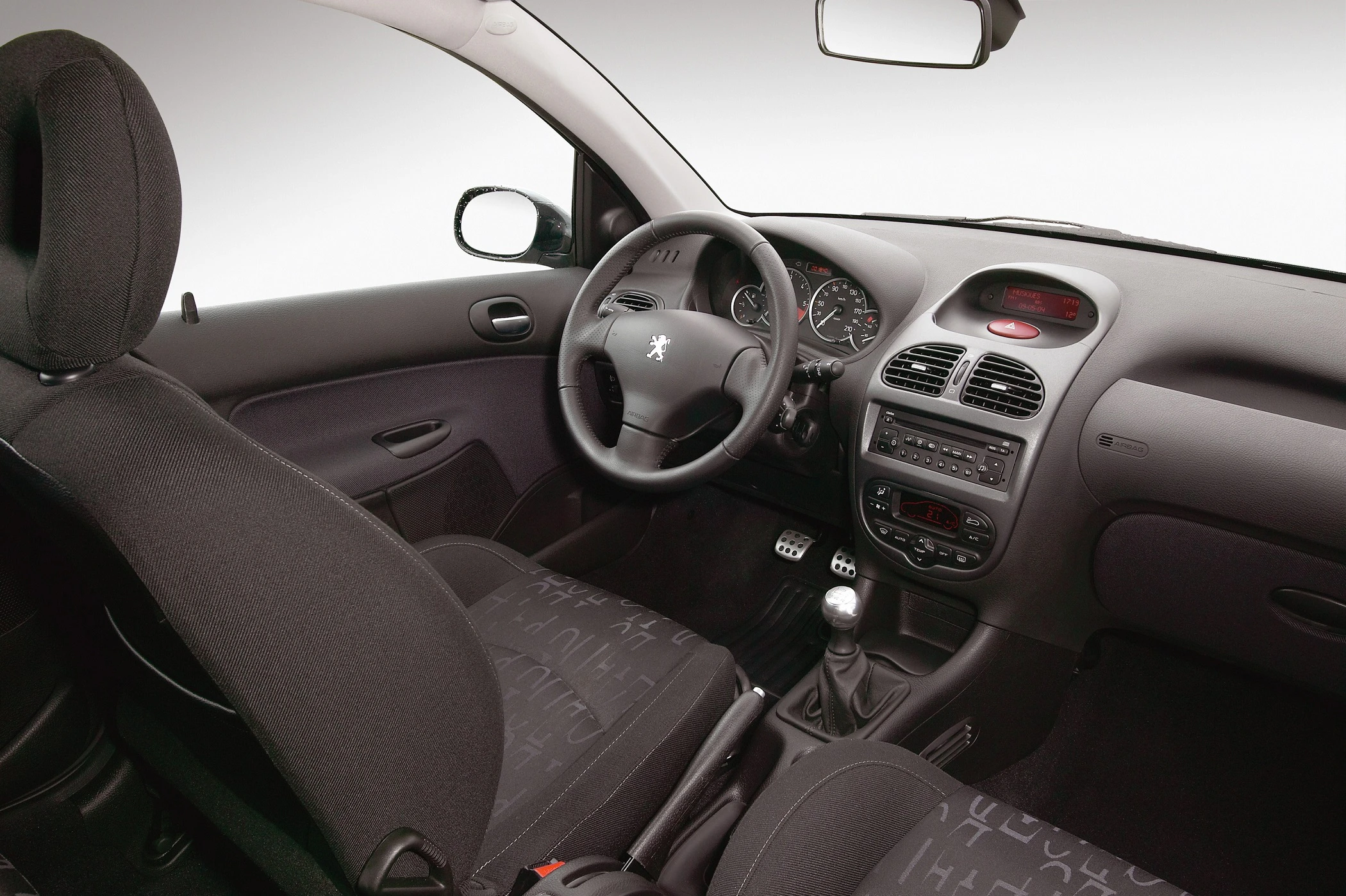 Innenraum eines Autos mit schwarzem Interieur, manuellem Schaltgetriebe und einem Peugeot-Logo auf dem Lenkrad.