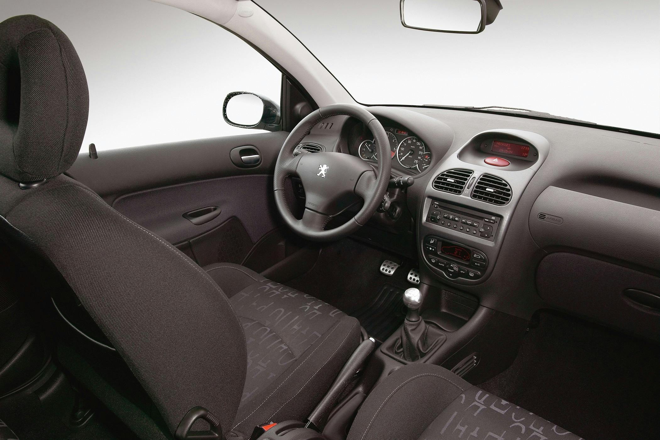 Innenraum eines Autos mit schwarzem Interieur, manuellem Schaltgetriebe und einem Peugeot-Logo auf dem Lenkrad.