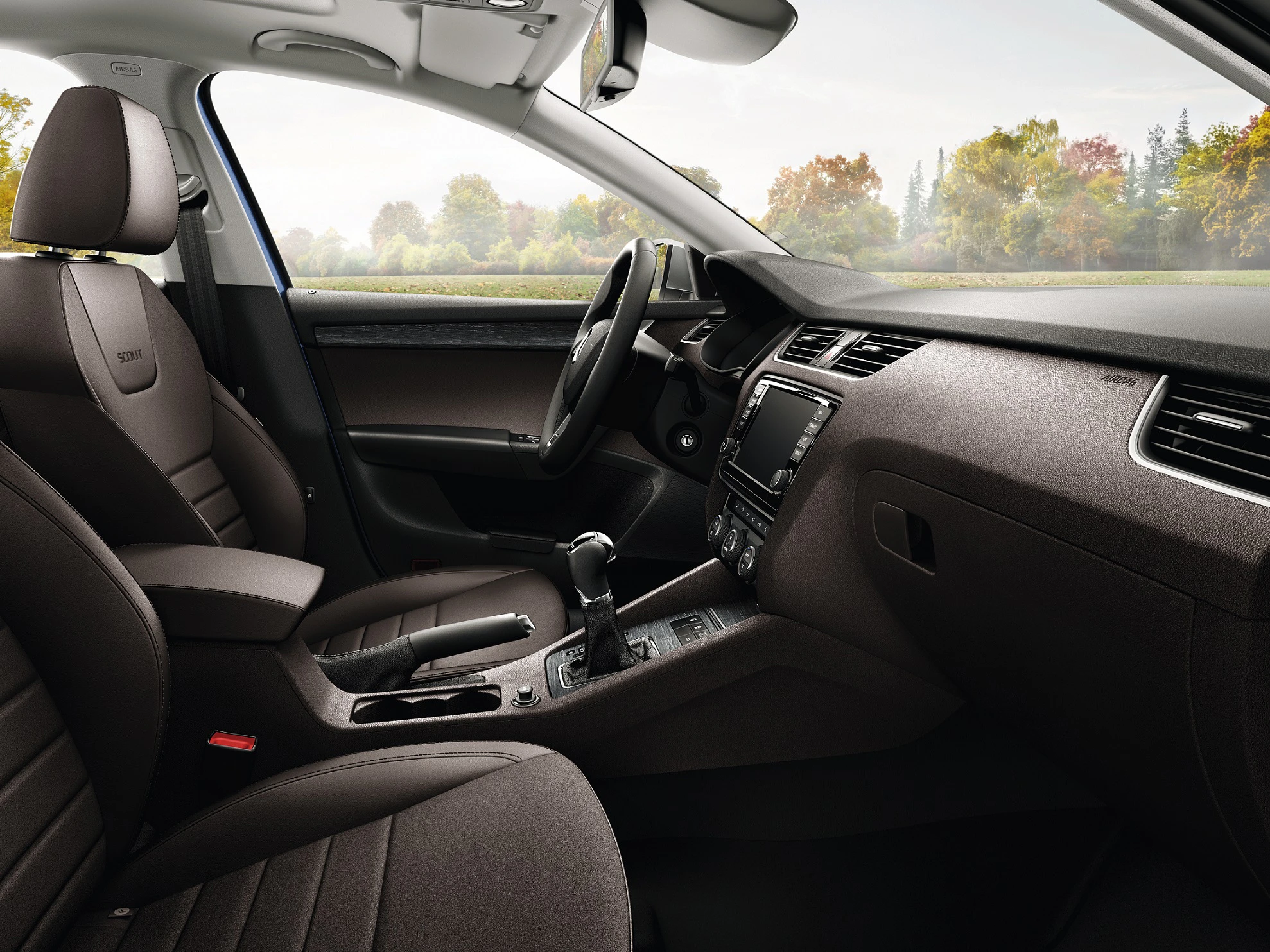 Innenraum eines modernen Autos mit braunen Ledersitzen und einem Blick auf das Armaturenbrett und Lenkrad. Im Hintergrund sind Bäume sichtbar.