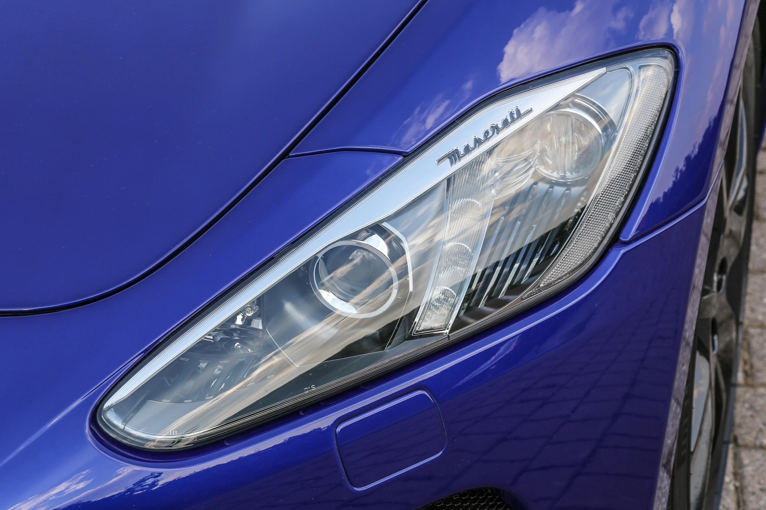 Nahaufnahme eines blauen Sportwagens mit einem markanten Frontscheinwerfer und dem Schriftzug "Maserati" darauf.