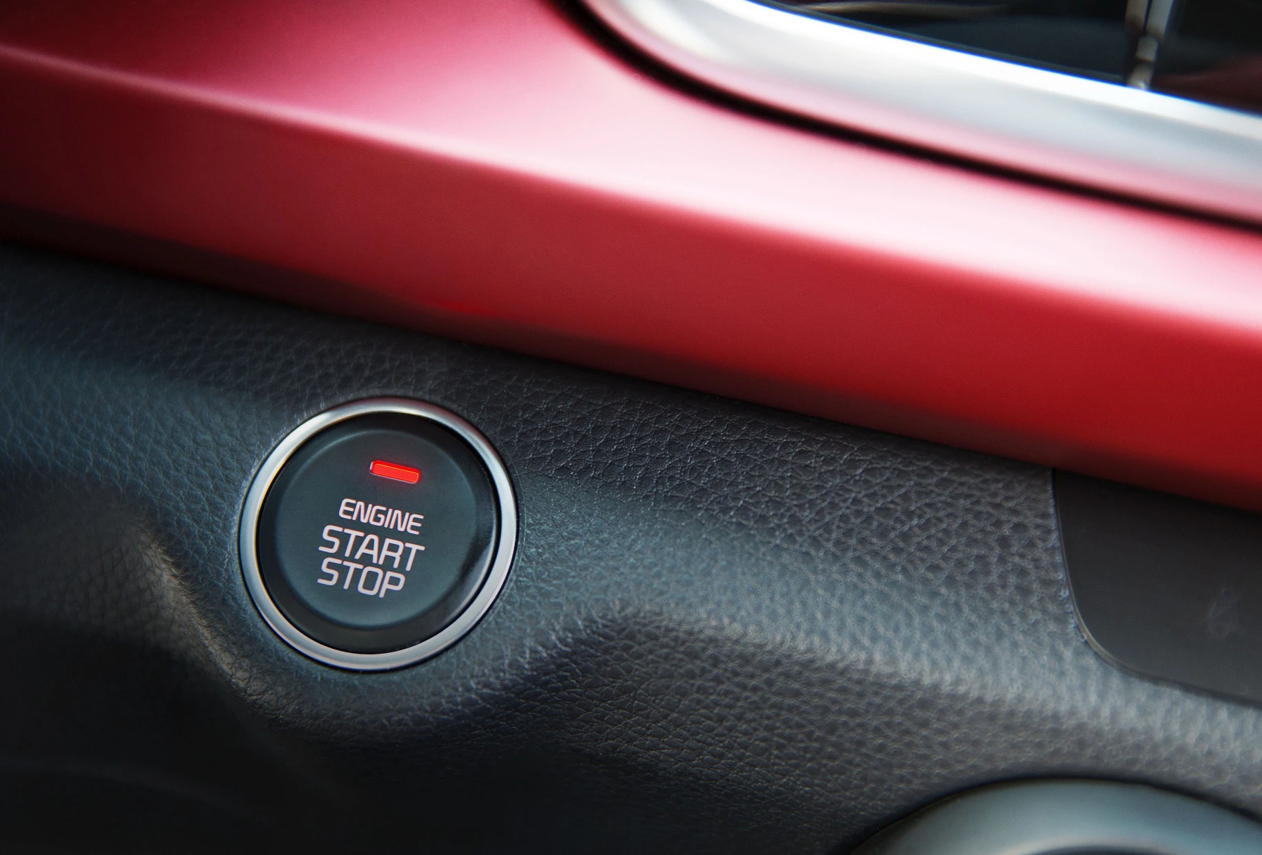 Nahaufnahme eines Autos mit rotem Start-Stopp-Knopf, umgeben von schwarzem und rotem Armaturenbrett.