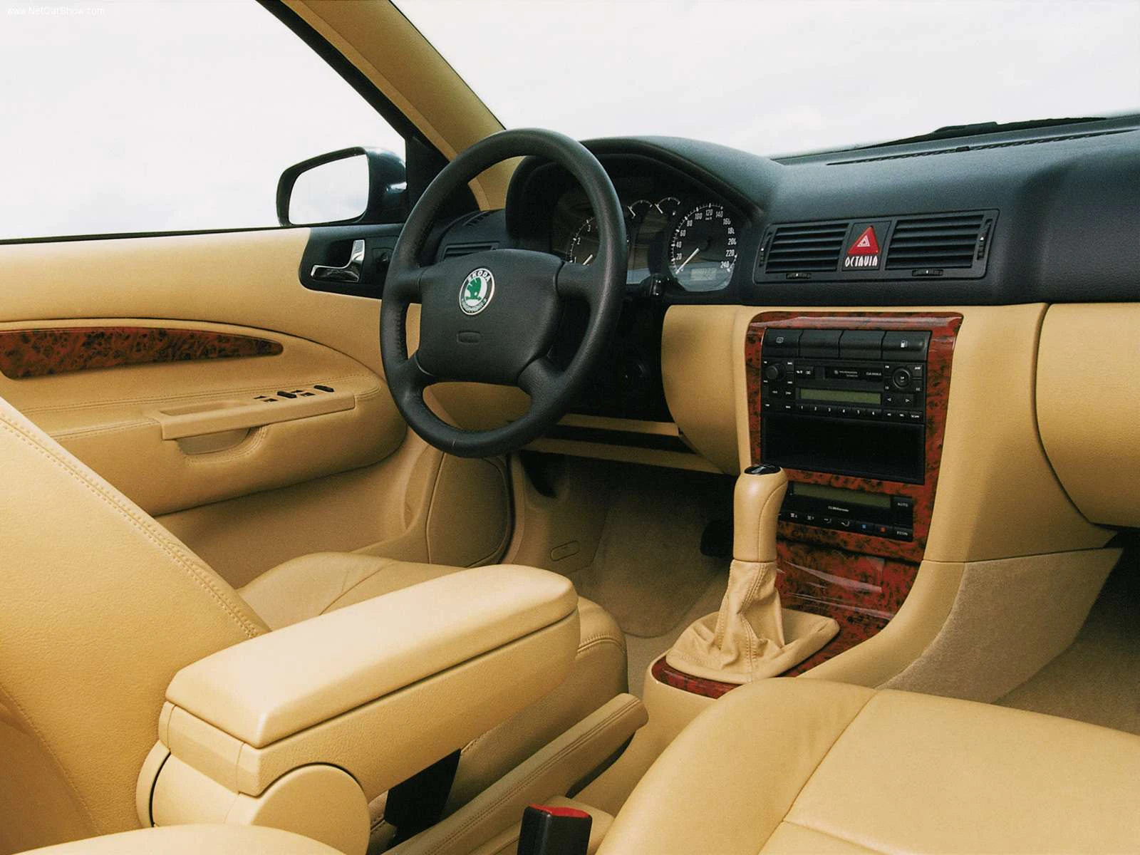 Innenraum eines Autos mit beigem Leder, Holzverkleidung, Lenkrad, Schalthebel und Armaturenbrett. Skoda-Logo am Lenkrad.