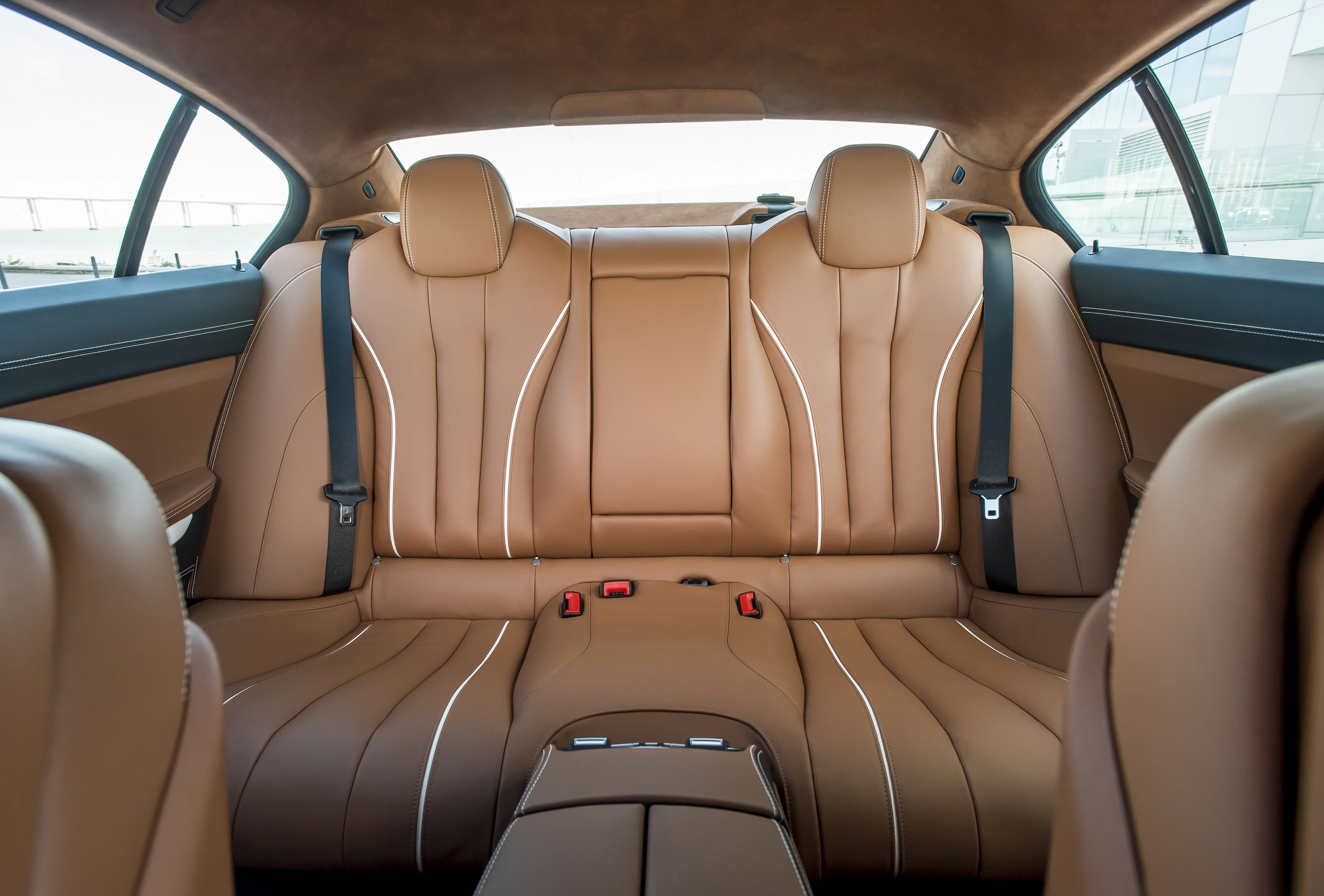 Brauner Ledersitzbereich eines Autos mit zwei Kopfstützen, mittlerem Armlehnenfach und Sicherheitsgurten, modernes Design.