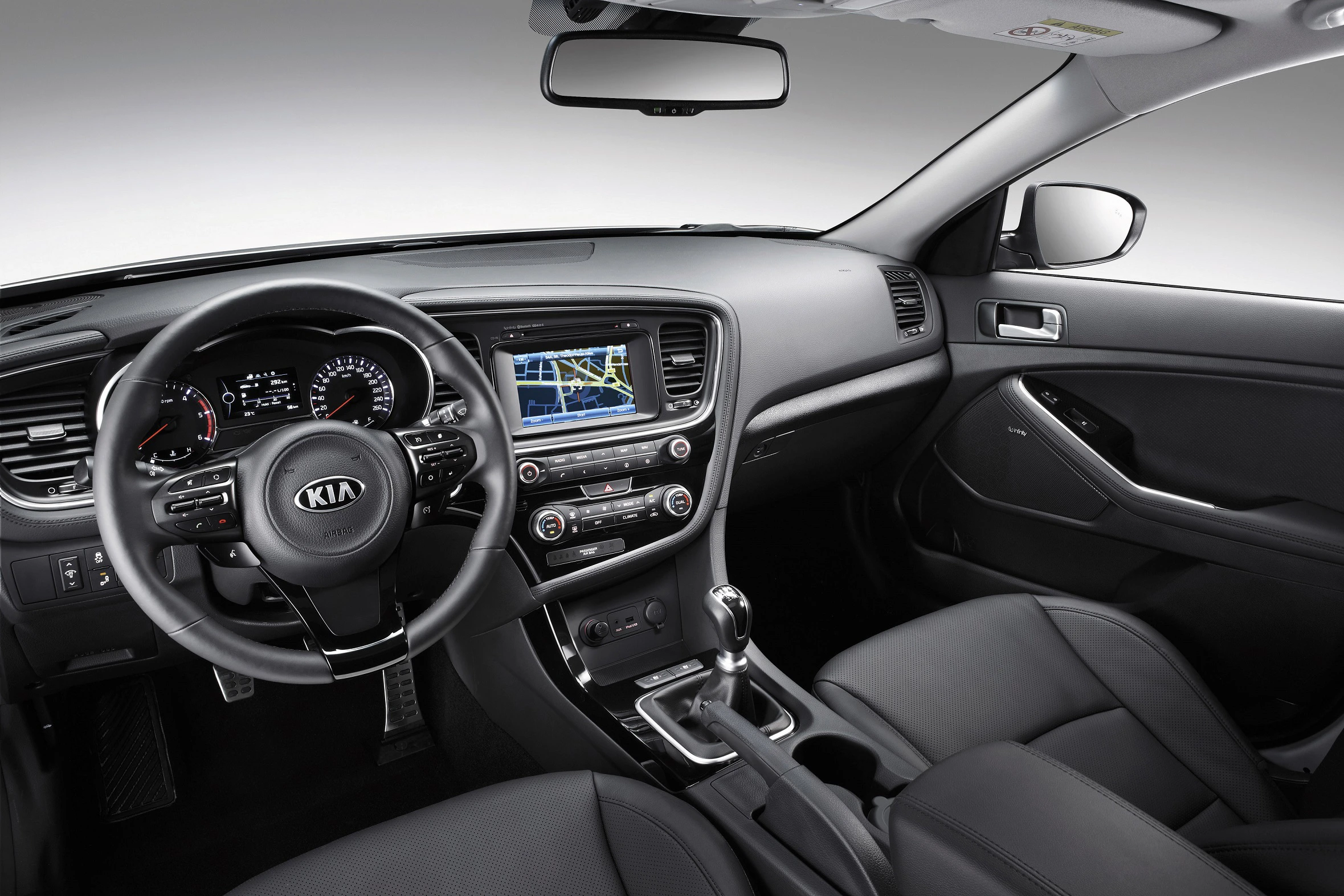 Innenraum eines modernen Autos mit Lederlenkrad, Touchscreen-Navigationssystem und Klimaanlagensteuerung, Armaturenbrett mit Kia-Logo.
