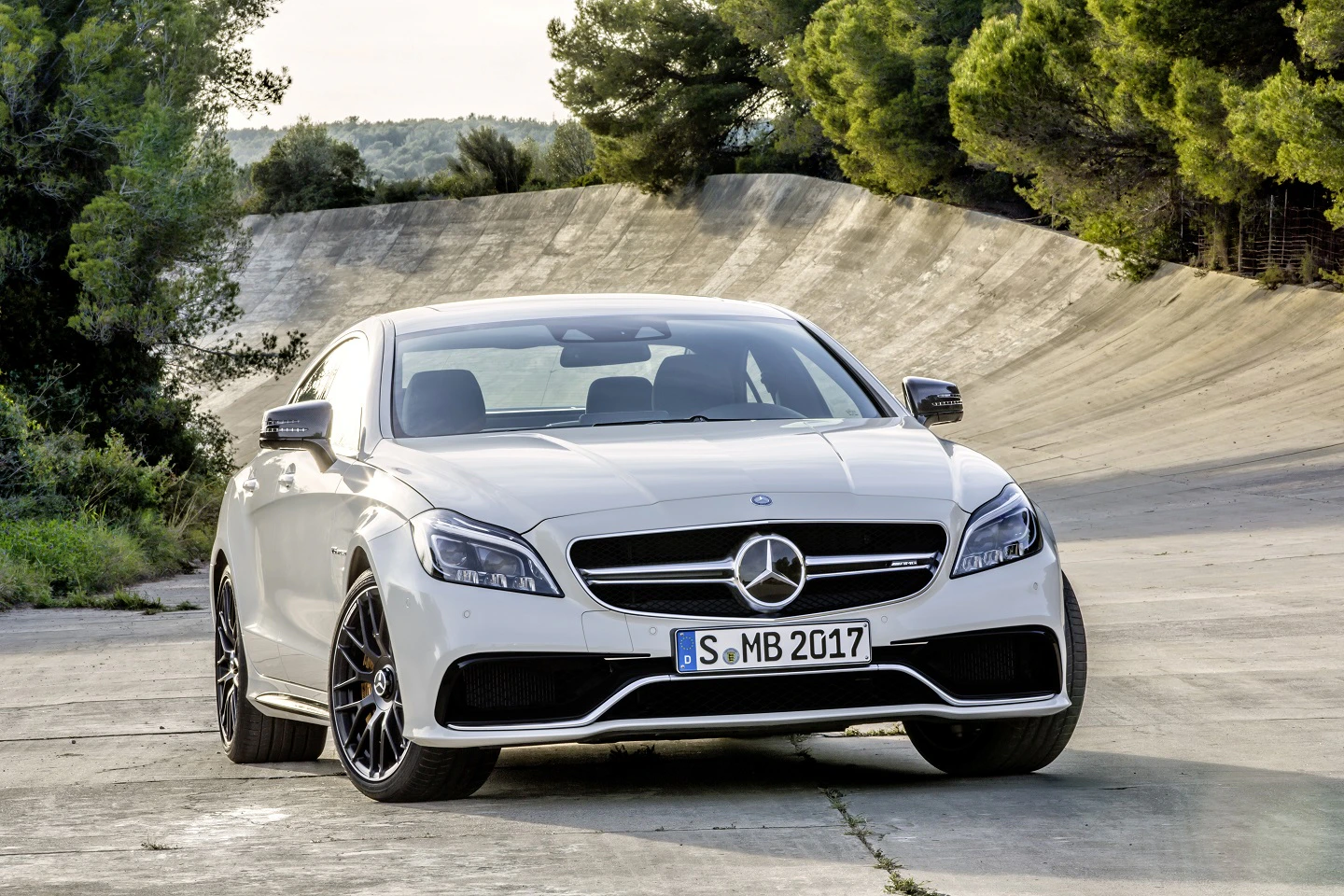 Weißer Mercedes-Benz auf kurviger Straße in Waldlandschaft, Ansicht von vorn.