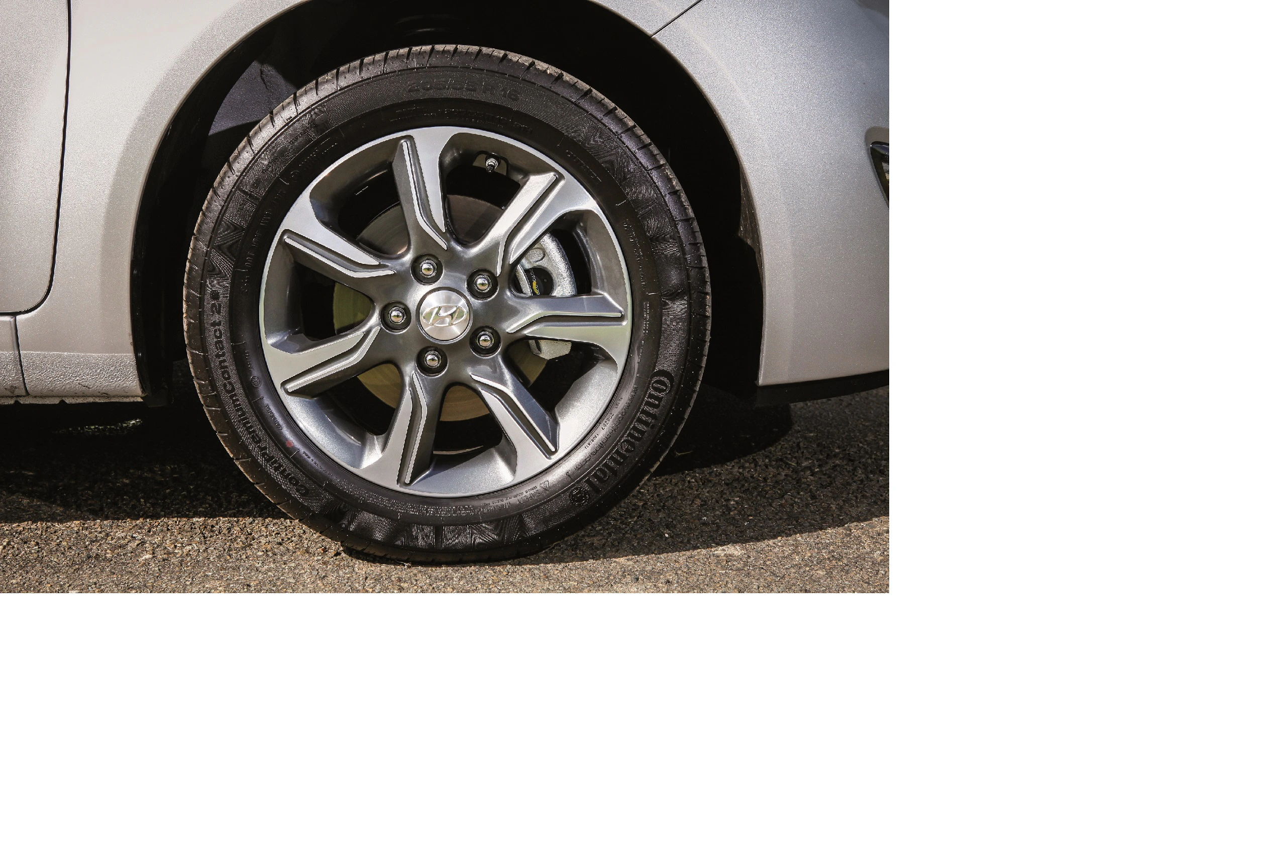 Nahaufnahme eines silbernen Autos mit Fokus auf die Vorderreifen und Alufelge, die auf einer asphaltierten Straße steht.