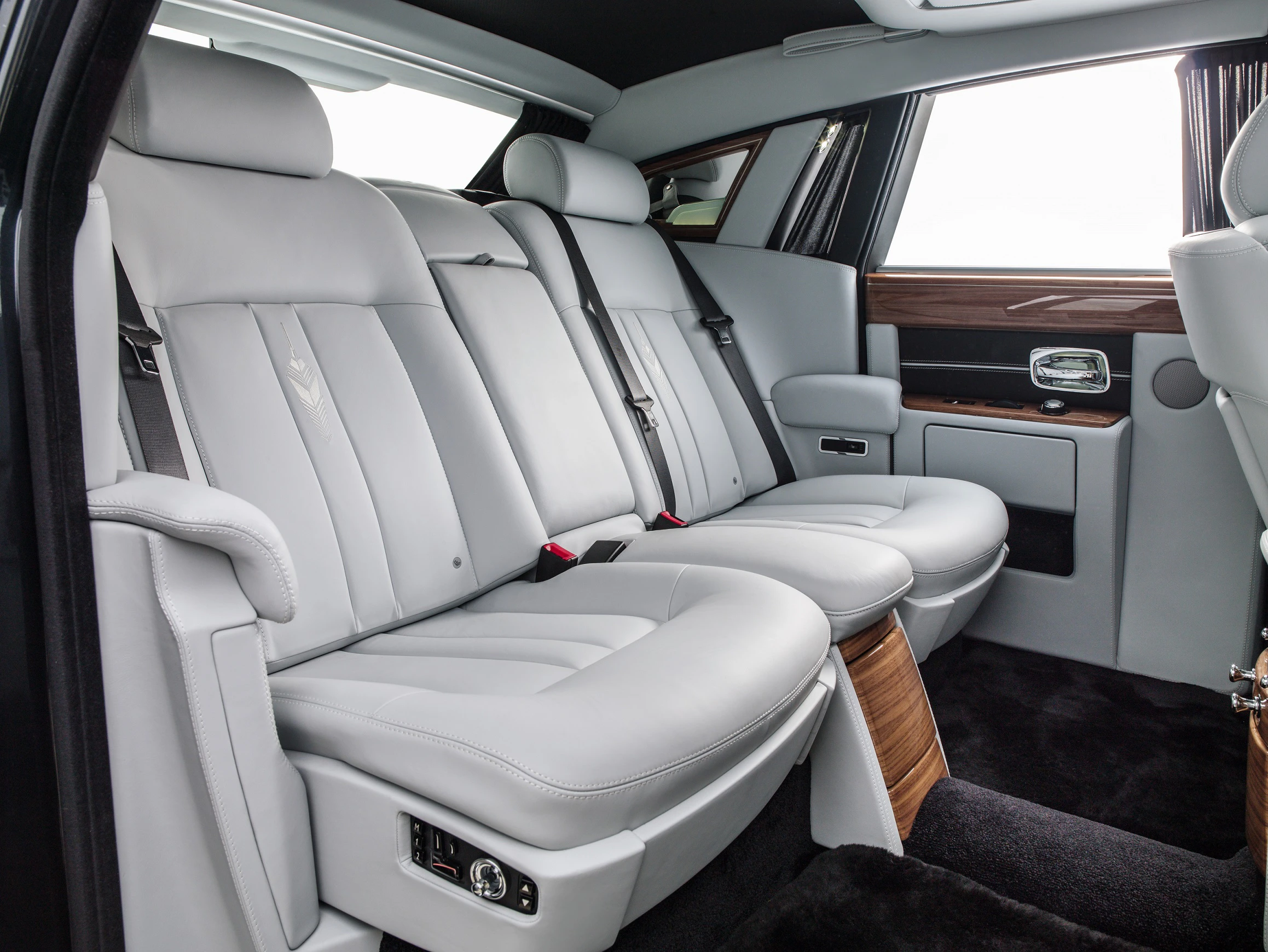 Luxuriöser Fahrzeuginnenraum mit hellgrauen Ledersitzen, Holzverkleidungen und eleganten Designelementen, gedeckte Beleuchtung.