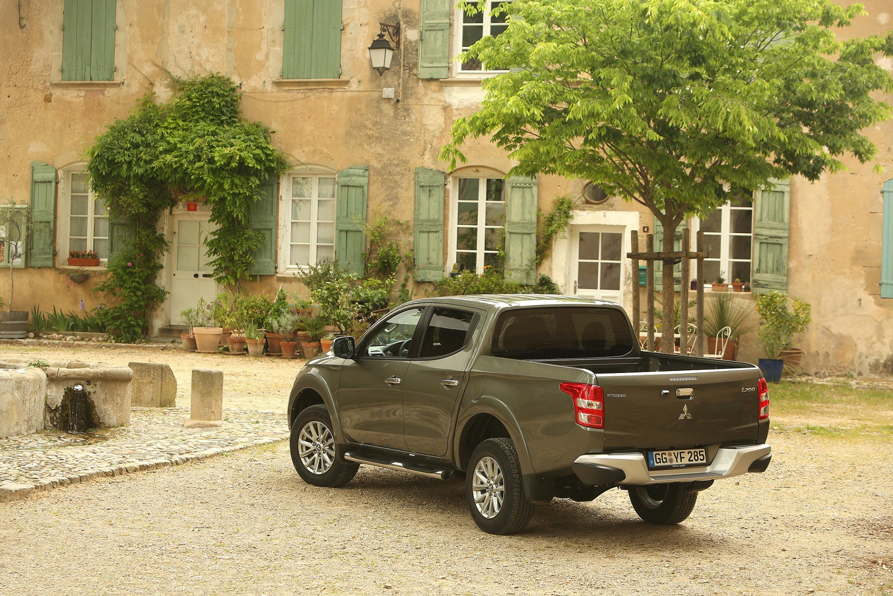 Ein grauer Pickup-Truck parkt vor einem historischen Gebäude mit grünen Fensterläden und Pflanzen auf einem gepflasterten Platz.