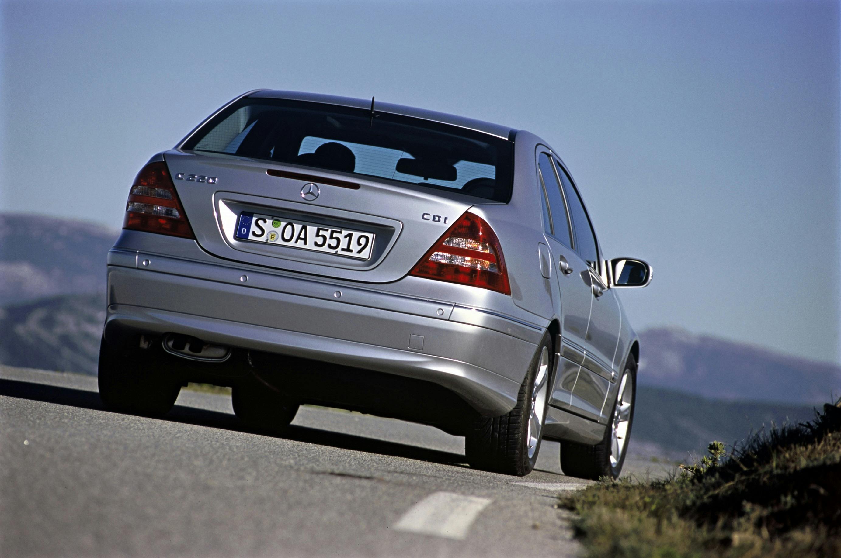 Silberner Mercedes-Benz C-Klasse CDI von hinten auf einer Landstraße, vor einer hügeligen Landschaft unter blauem Himmel.