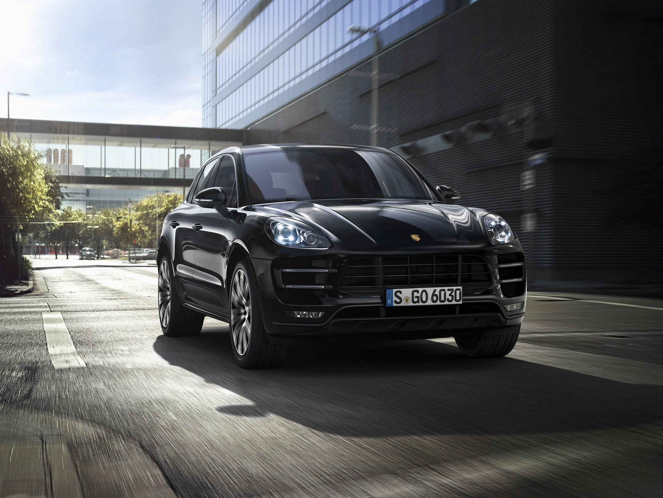 Schwarzes Auto fährt tagsüber auf einer urbanen Straße. Gebäude und Bäume im Hintergrund, modernes und dynamisches Design.