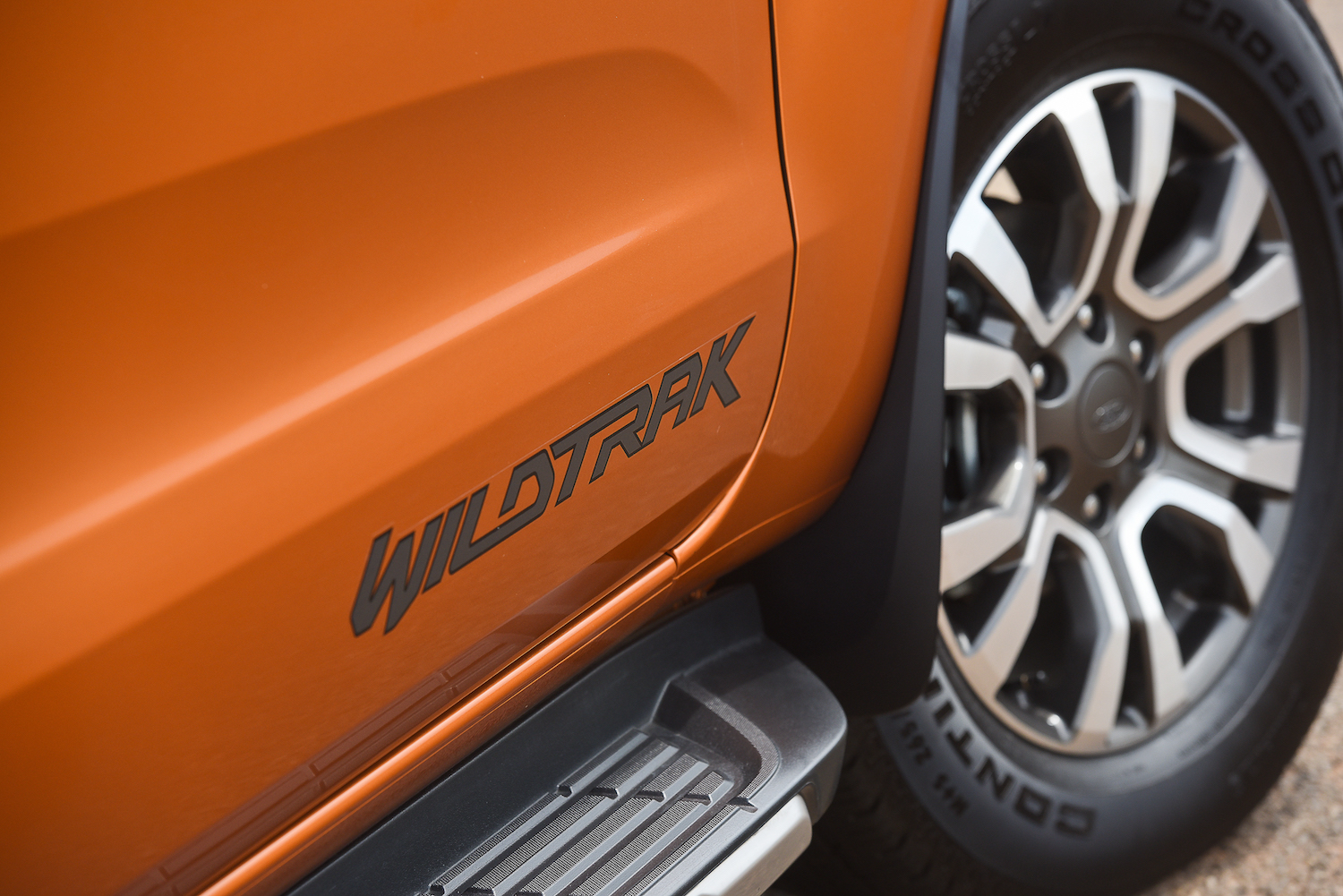 Nahaufnahme eines orangefarbenen Fahrzeugs, das "Wildtrak" auf der Seite zeigt, mit sichtbarem Reifen und Trittbrett.
