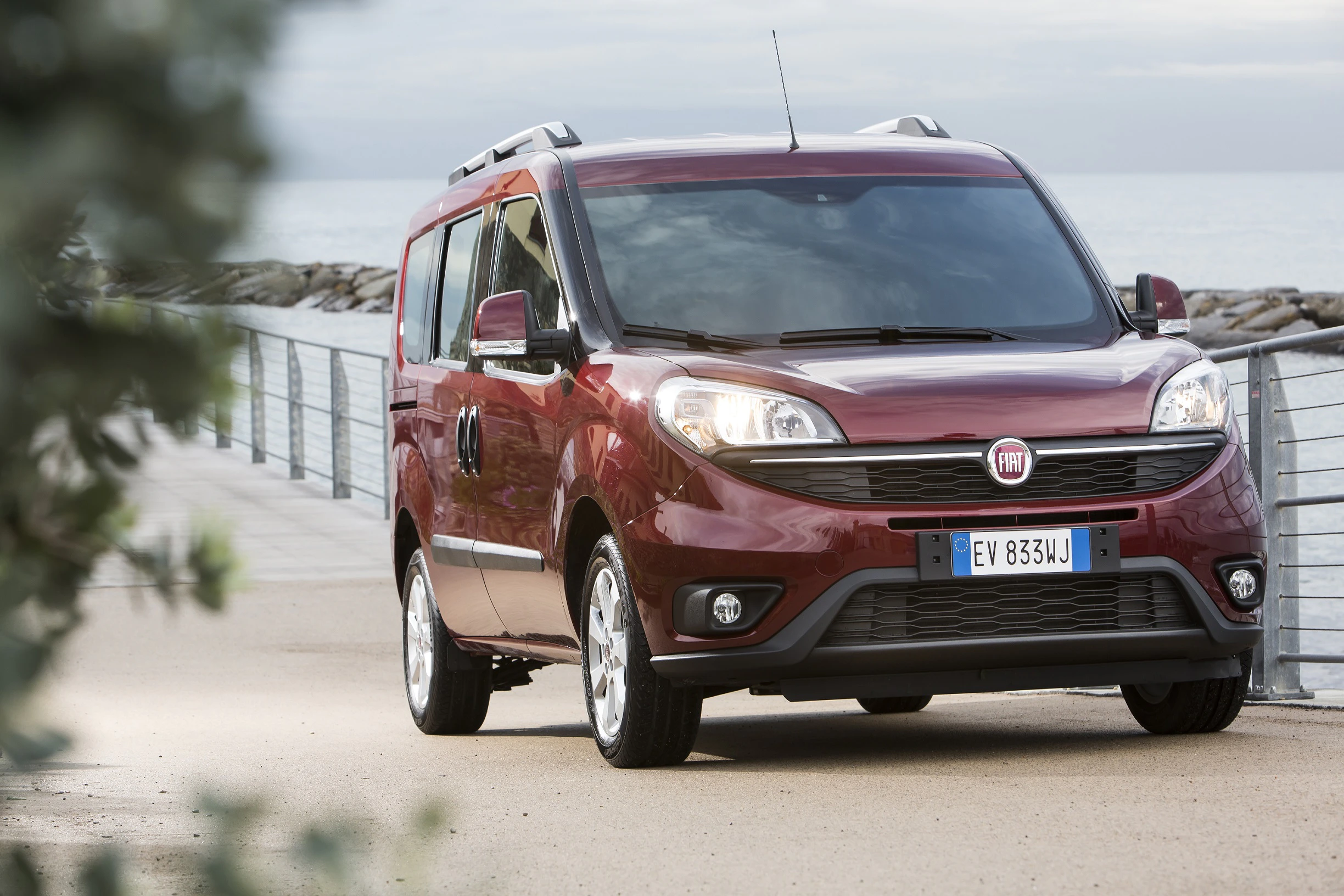Roter Fiat-Van parkt auf einer Promenade mit Meerblick im Hintergrund, ein moderner und funktionaler Familienwagen.