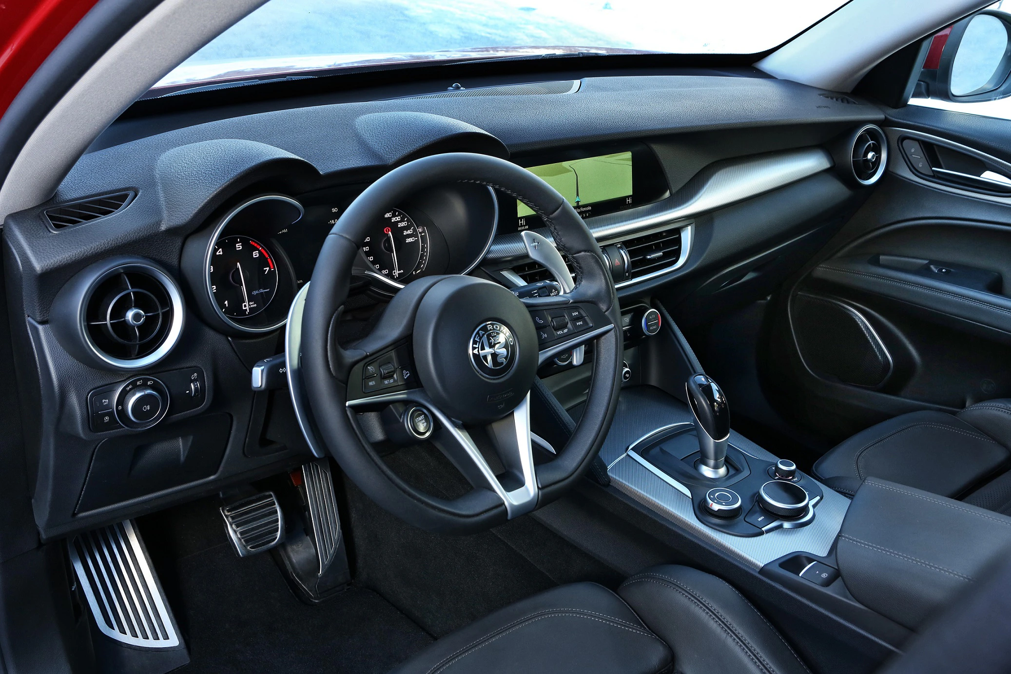 Innenraum eines Autos mit modernem Lenkrad, Instrumententafel, Touchscreen, Lüftungsdüsen und schwarzen Ledersitzen.