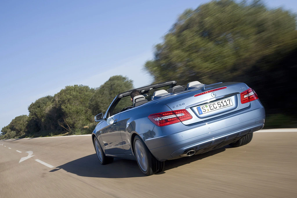 Blaues Cabrio fährt auf Landstraße, umgeben von Bäumen. Das Auto hat ein geöffnetes Verdeck. Nummernschild: S-EC 5117.