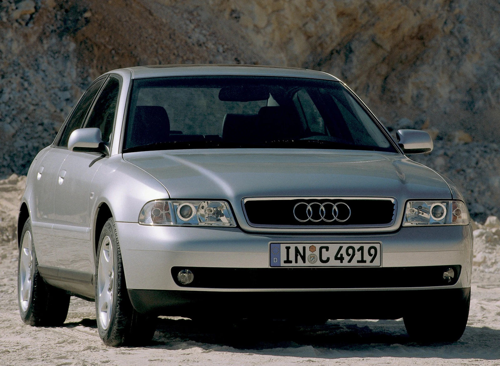 Silberner Audi A4 vor einem felsigen Hintergrund, frontal aufgenommen. Das Auto hat runde Scheinwerfer und ein typisches Audi-Emblem.