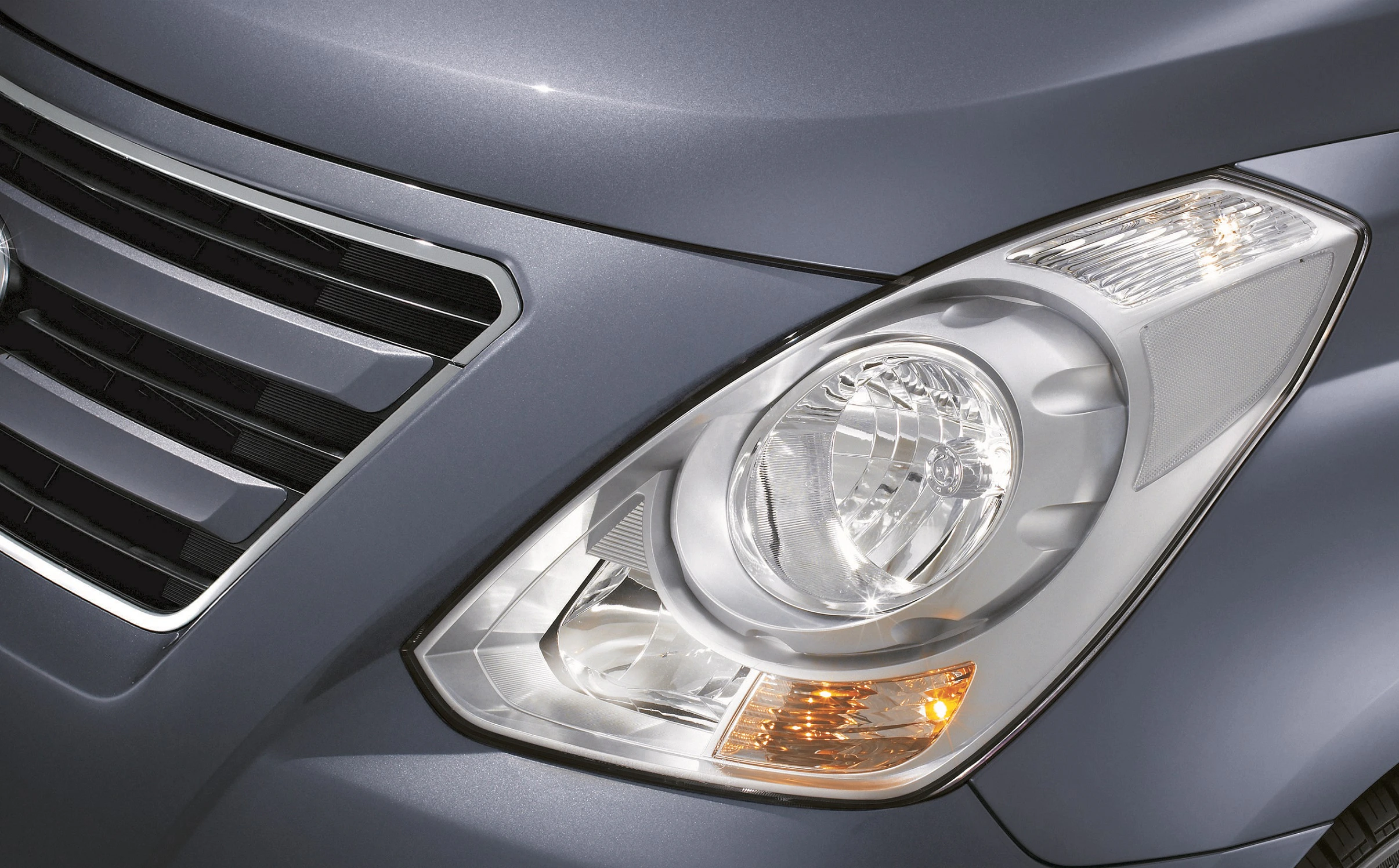 Nahaufnahme eines Autoscheinwerfers und Kühlergrills eines grauen Fahrzeugs. Die Details der Lichtreflexion und des Designs sind sichtbar.