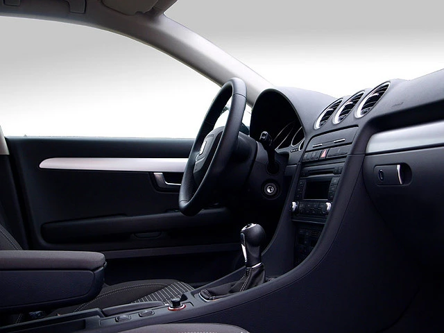 Innenraum eines modernen Autos mit schwarzem Lenkrad, Schalthebel und Armaturenbrett. Die Sitze sind schwarz und elegant gestaltet.