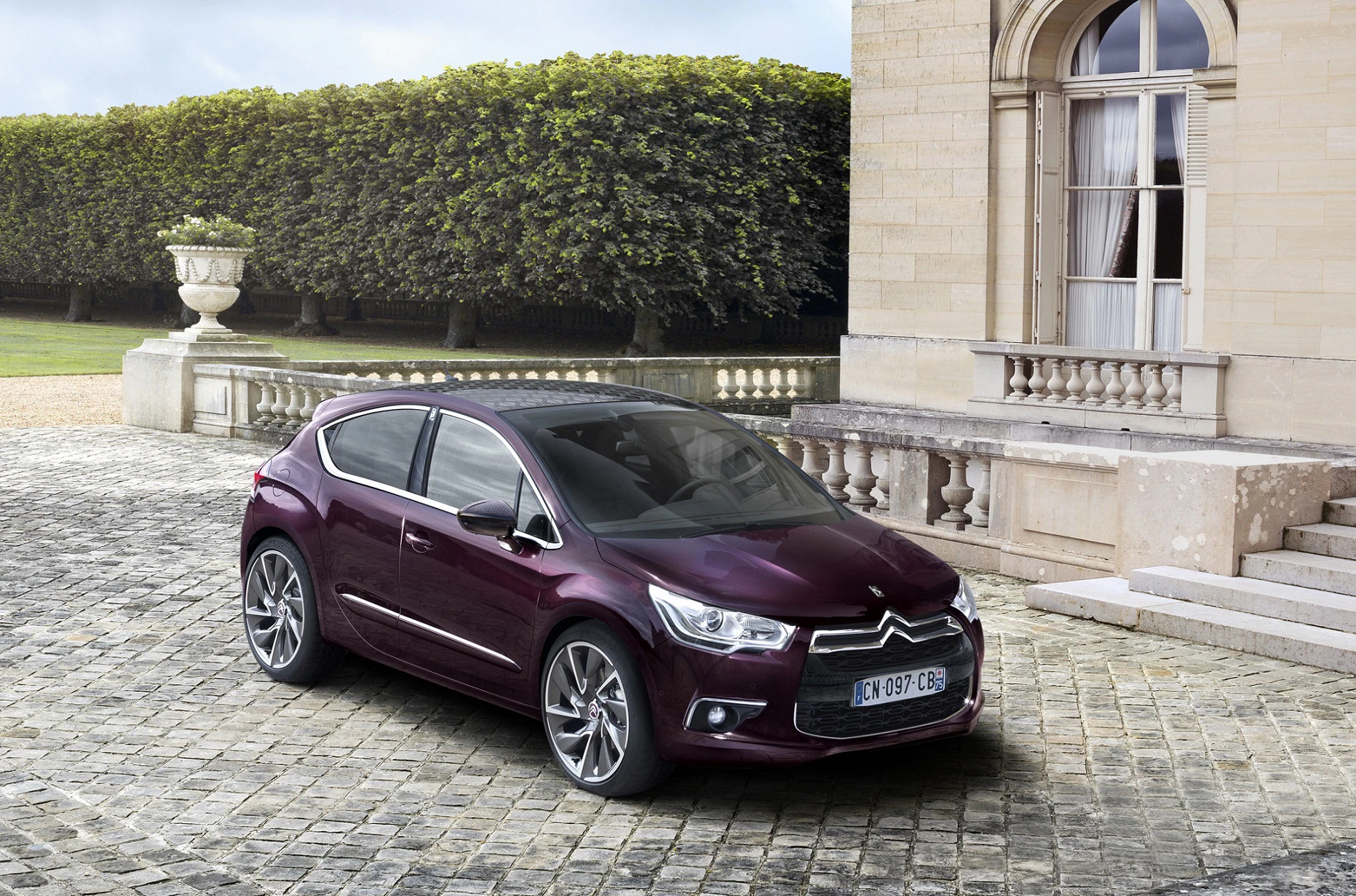 Lila Citroën DS5 steht auf gepflastertem Hof vor historischem Gebäude mit großen Fenstern und gepflegten Hecken im Hintergrund.
