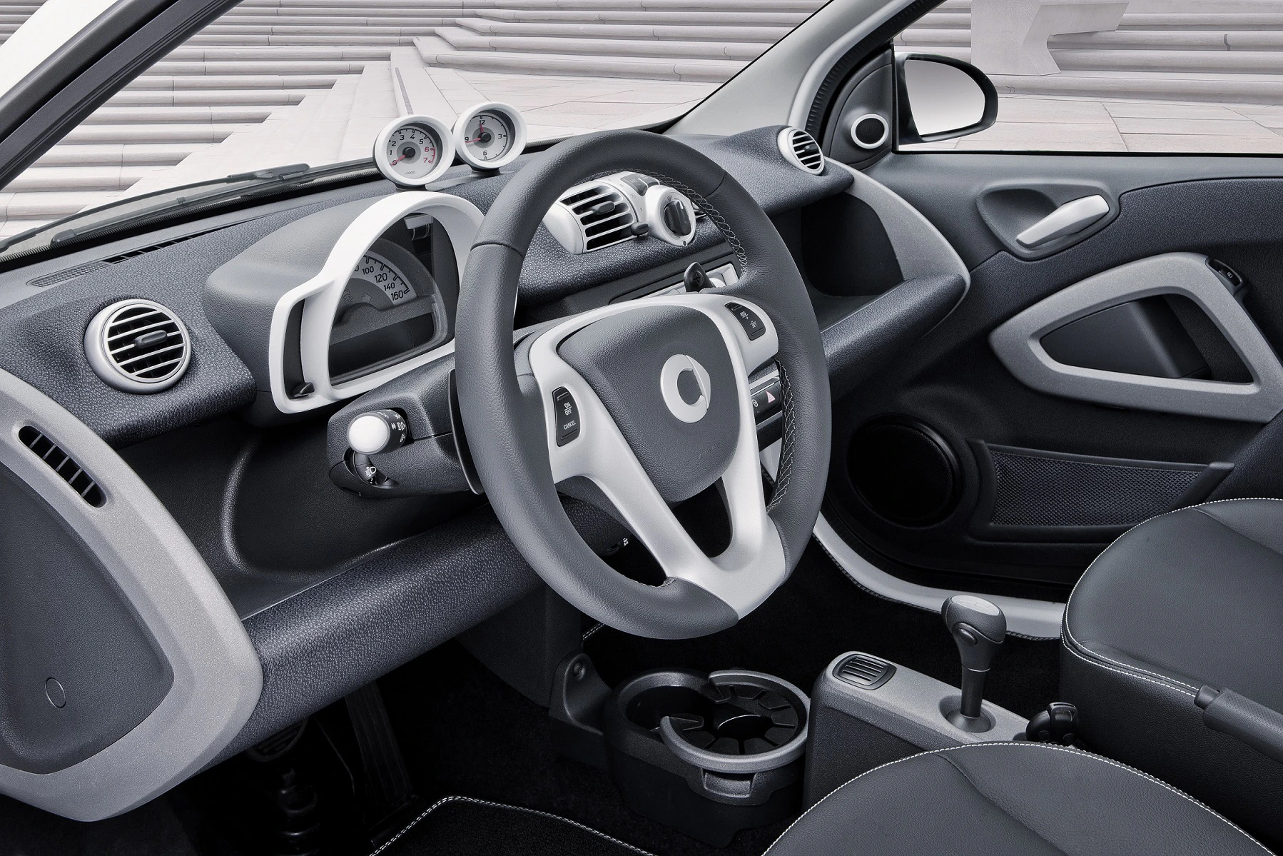 Modernes Autoinnenraumdesign mit grauem und schwarzem Armaturenbrett, kreisförmigen Lüftungsschlitzen und einem Multifunktionslenkrad.