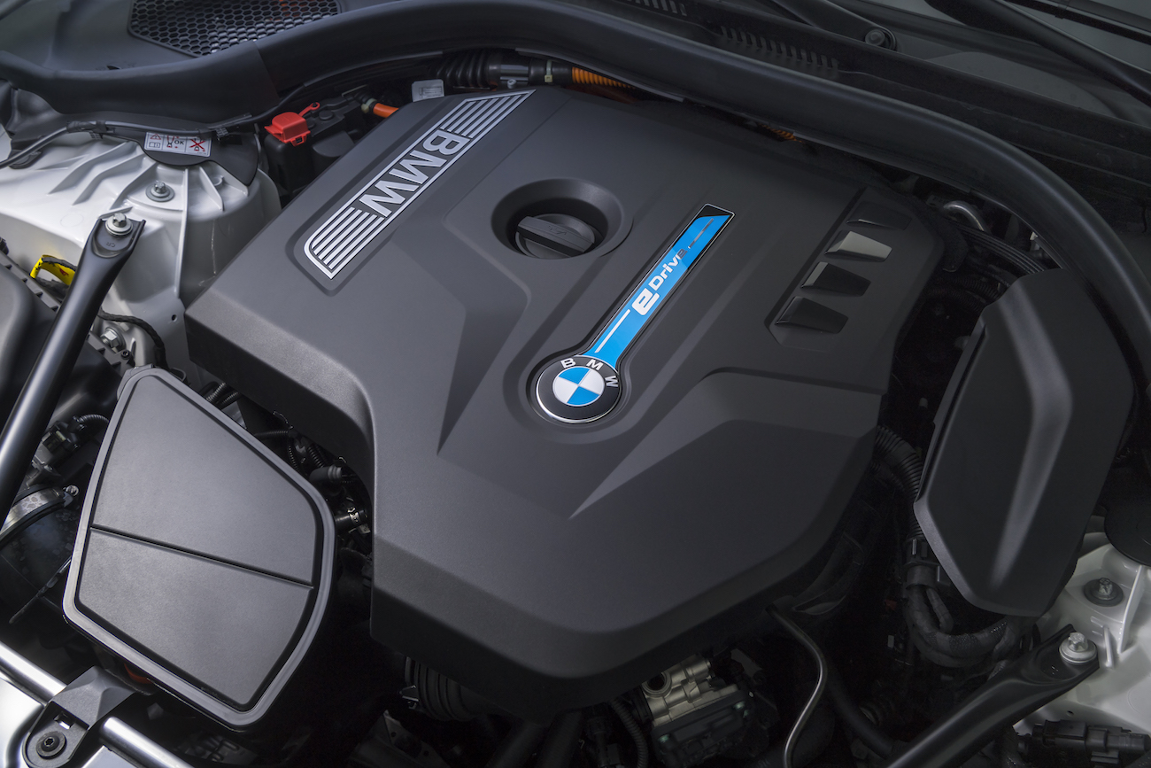 BMW-Motor mit schwarzer Abdeckung und blauem eDrive-Logo. Autoteile sind sichtbar im Motorraum.