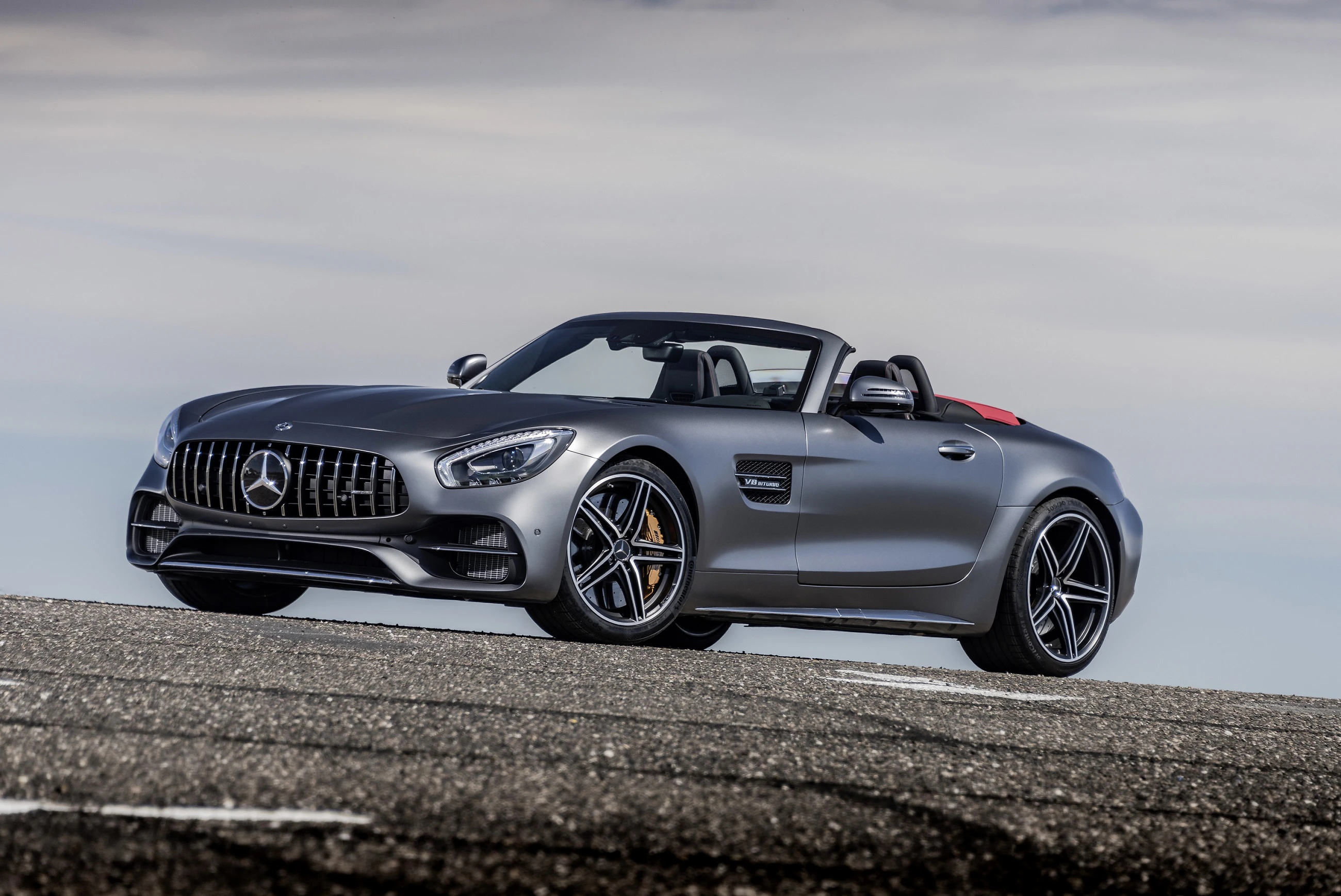 Graues Mercedes-Cabrio auf einer asphaltierten Straße, schräg von vorne fotografiert, mit bewölktem Himmel im Hintergrund.