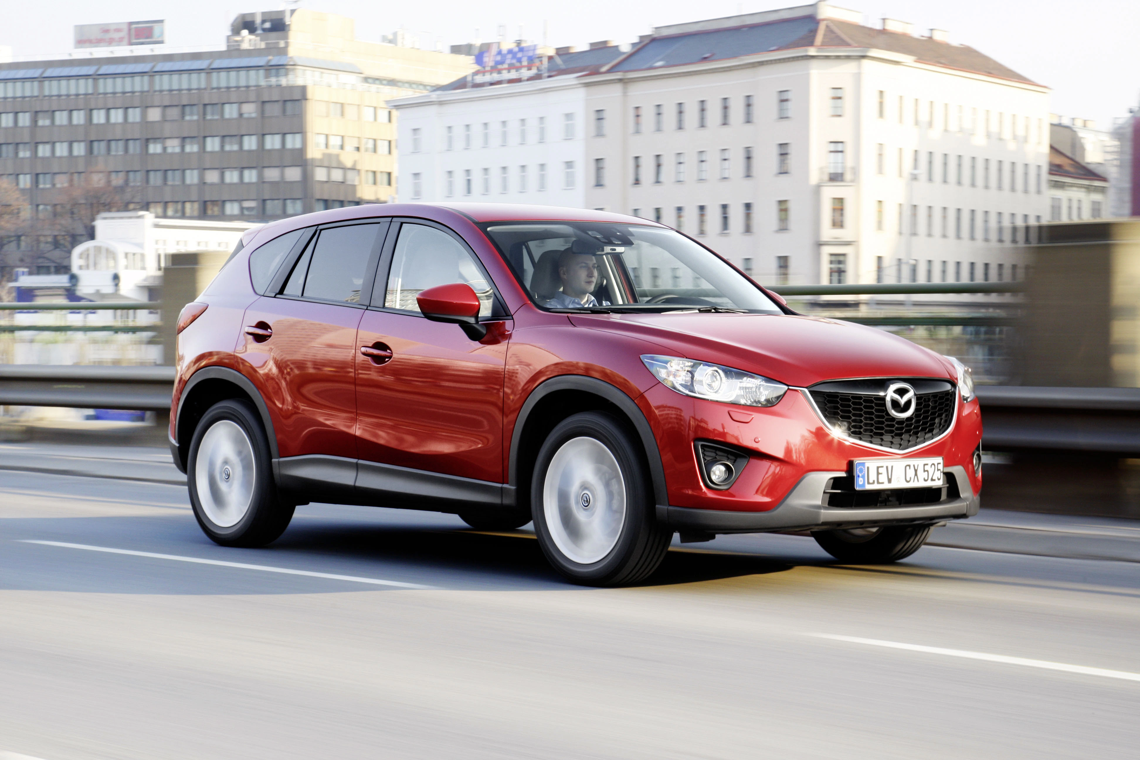 Roter Mazda CX-5 fährt auf einer Straße in der Stadt, im Hintergrund sind Gebäude zu sehen.