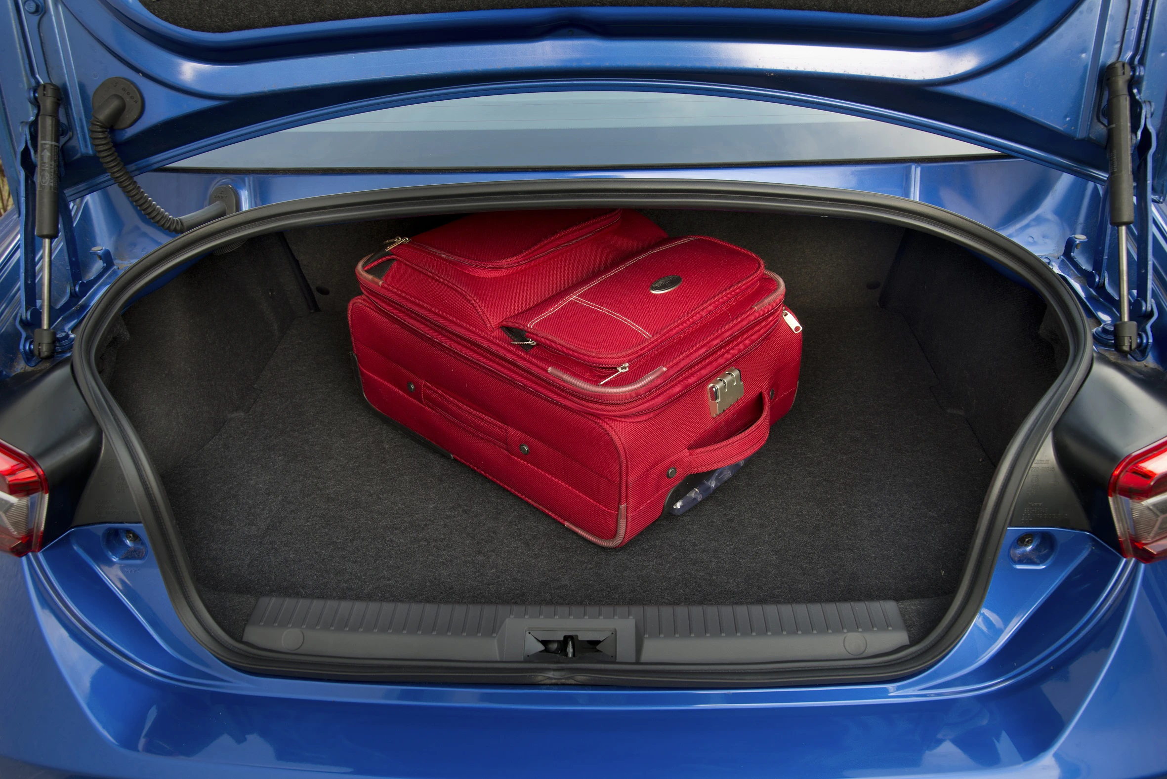 Ein roter Koffer liegt im geöffneten Kofferraum eines blauen Autos.