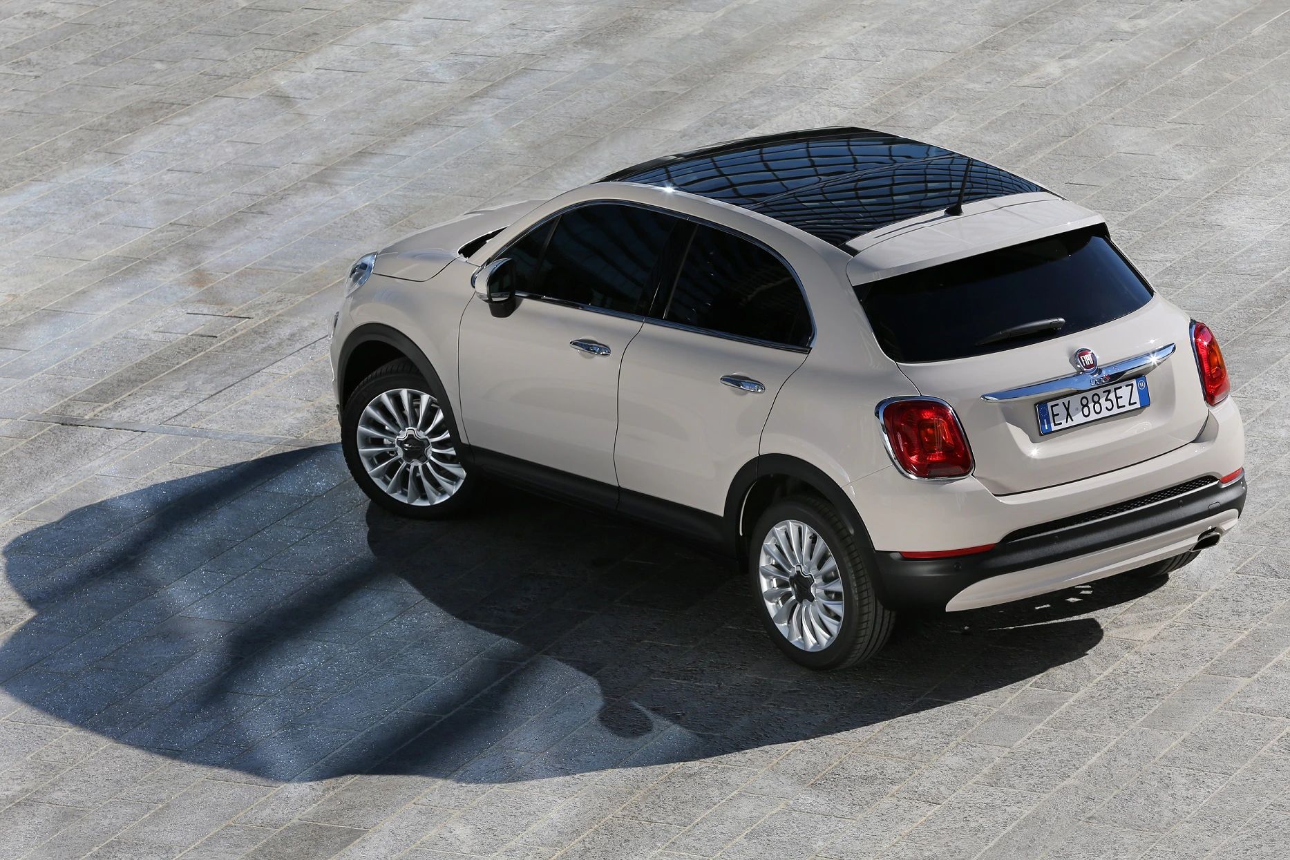 Beigefarbener SUV auf grauem Untergrund mit reflektierenden Schatten. Fahrzeug von oben fotografiert.