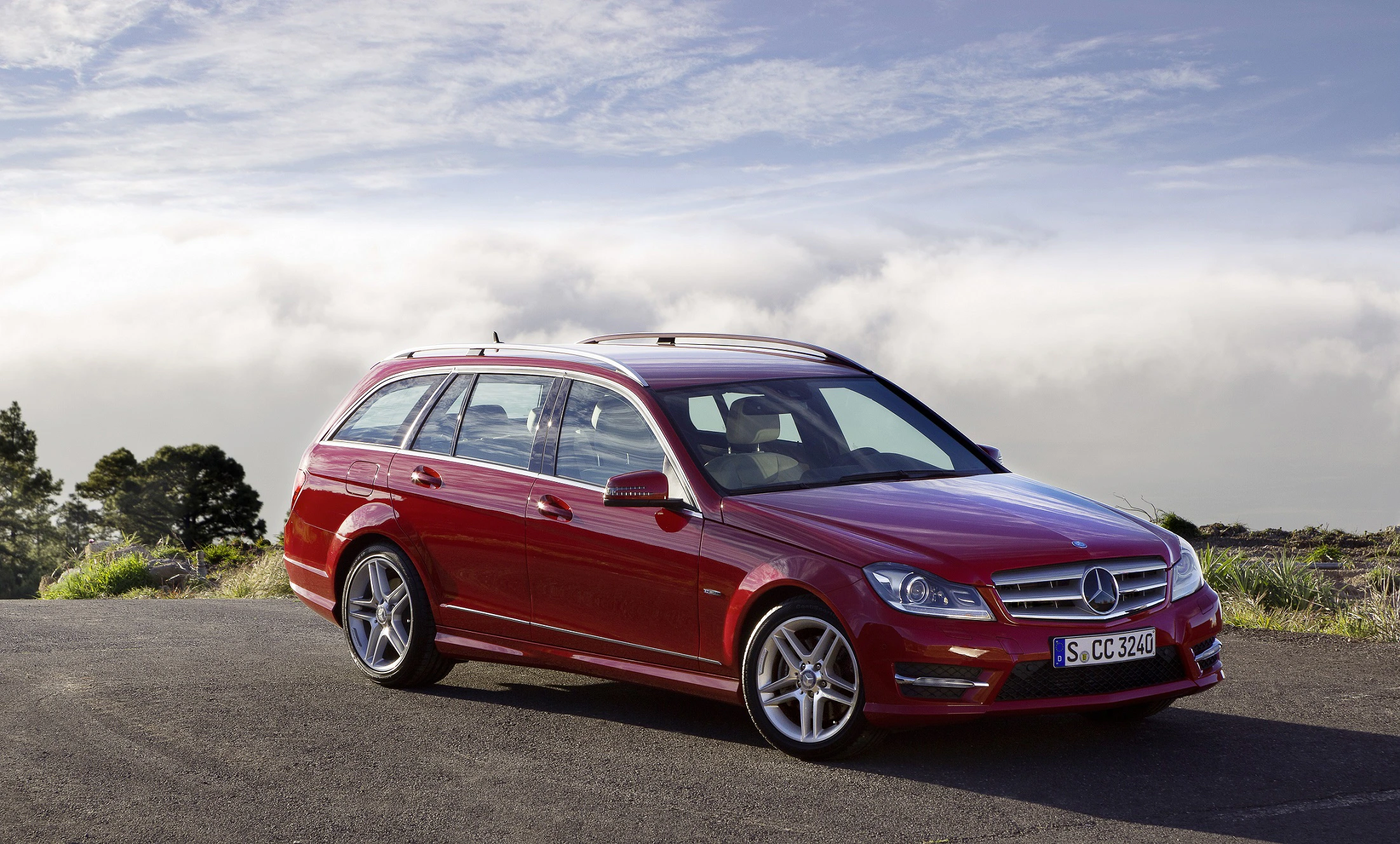 Roter Kombi Mercedes-Benz steht auf einer Straße, im Hintergrund Bäume und bewölkter Himmel.