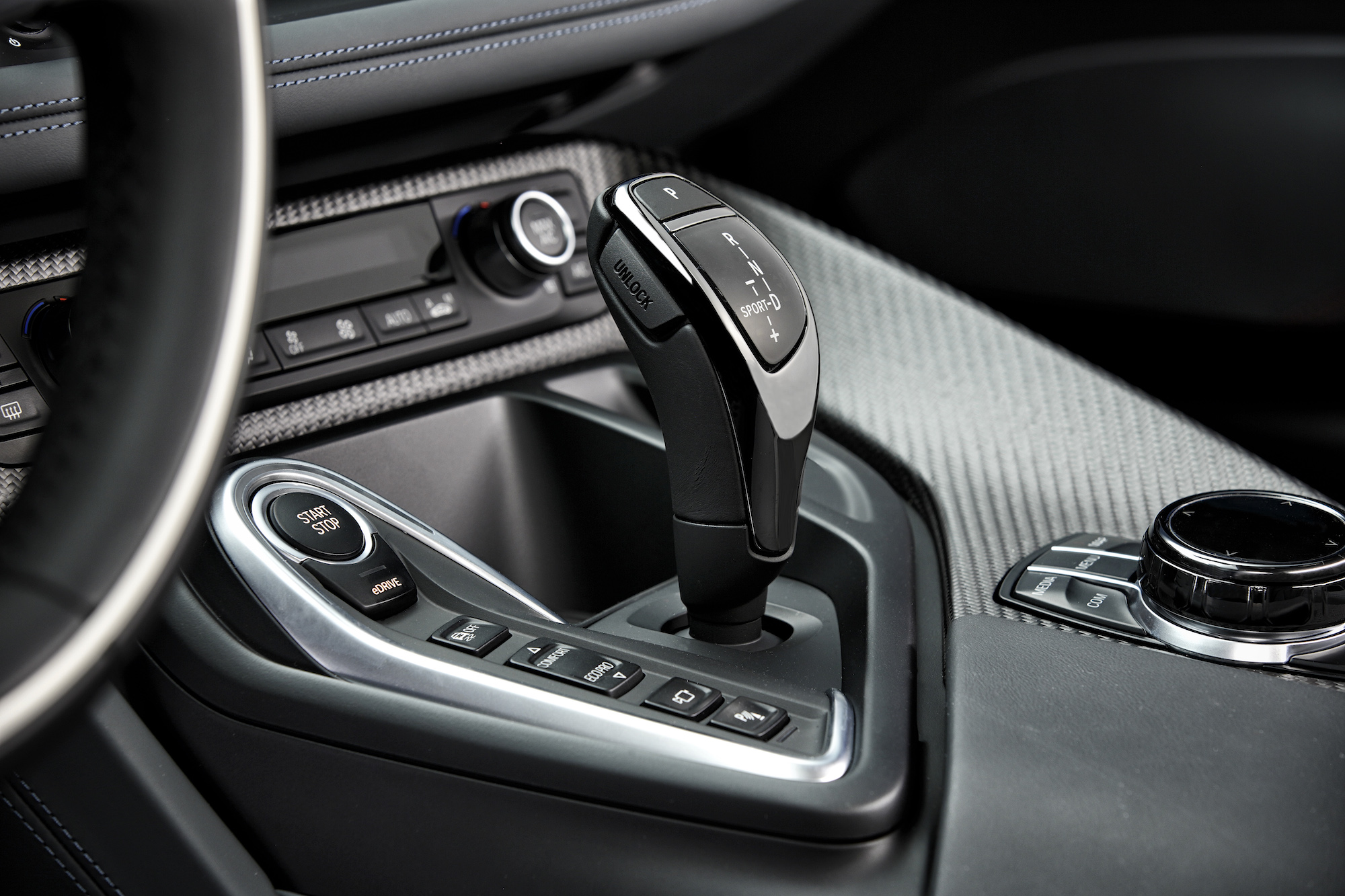 Nahaufnahme eines modernen Automatikgetriebes in einem Auto, umgeben von Bedienelementen und einem drehbaren Auswahlknopf.