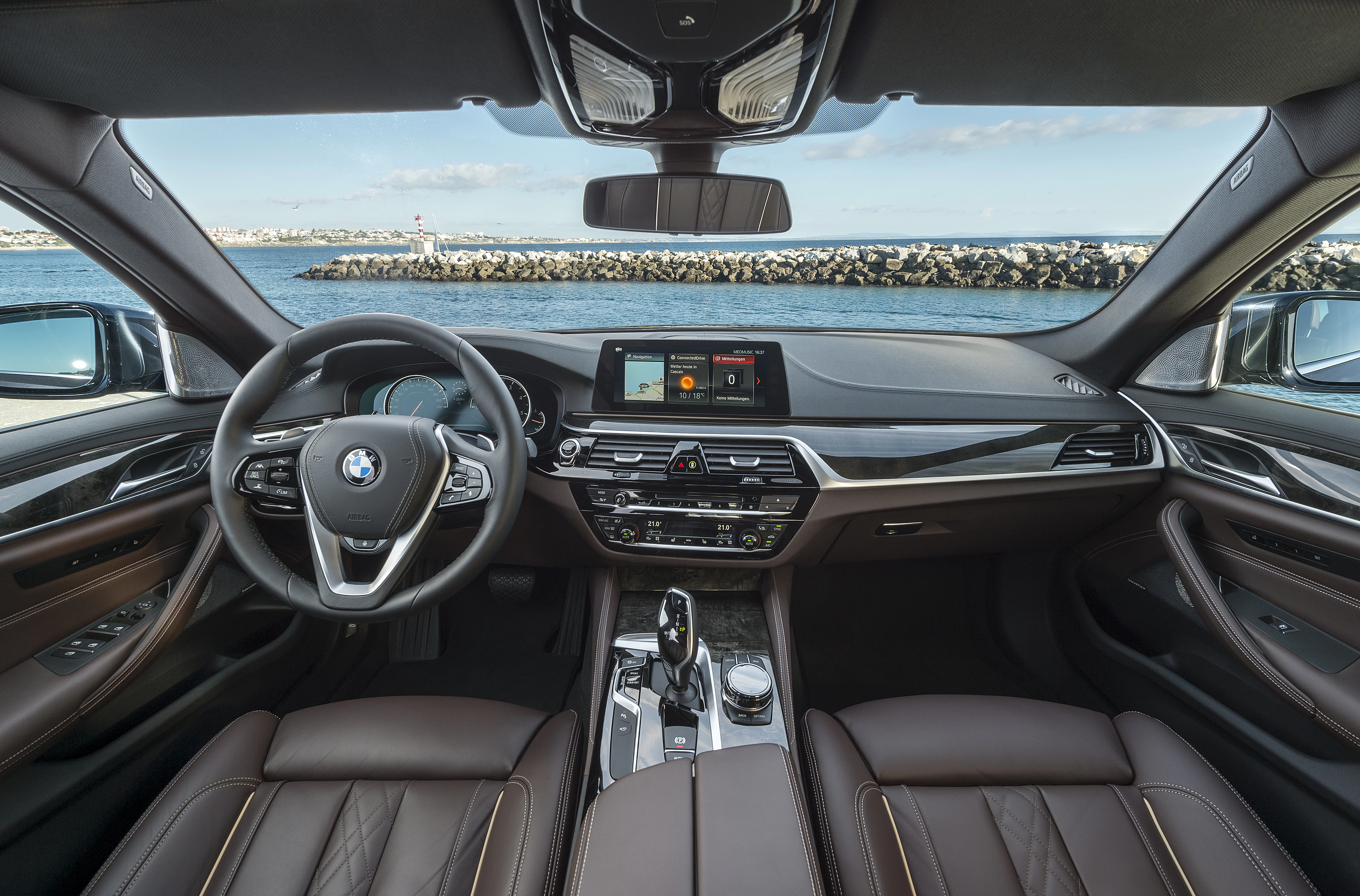 Innenraum eines modernen BMW-Autos mit Lederpolstern und digitalem Armaturenbrett. Meerblick durch die Windschutzscheibe im Hintergrund.